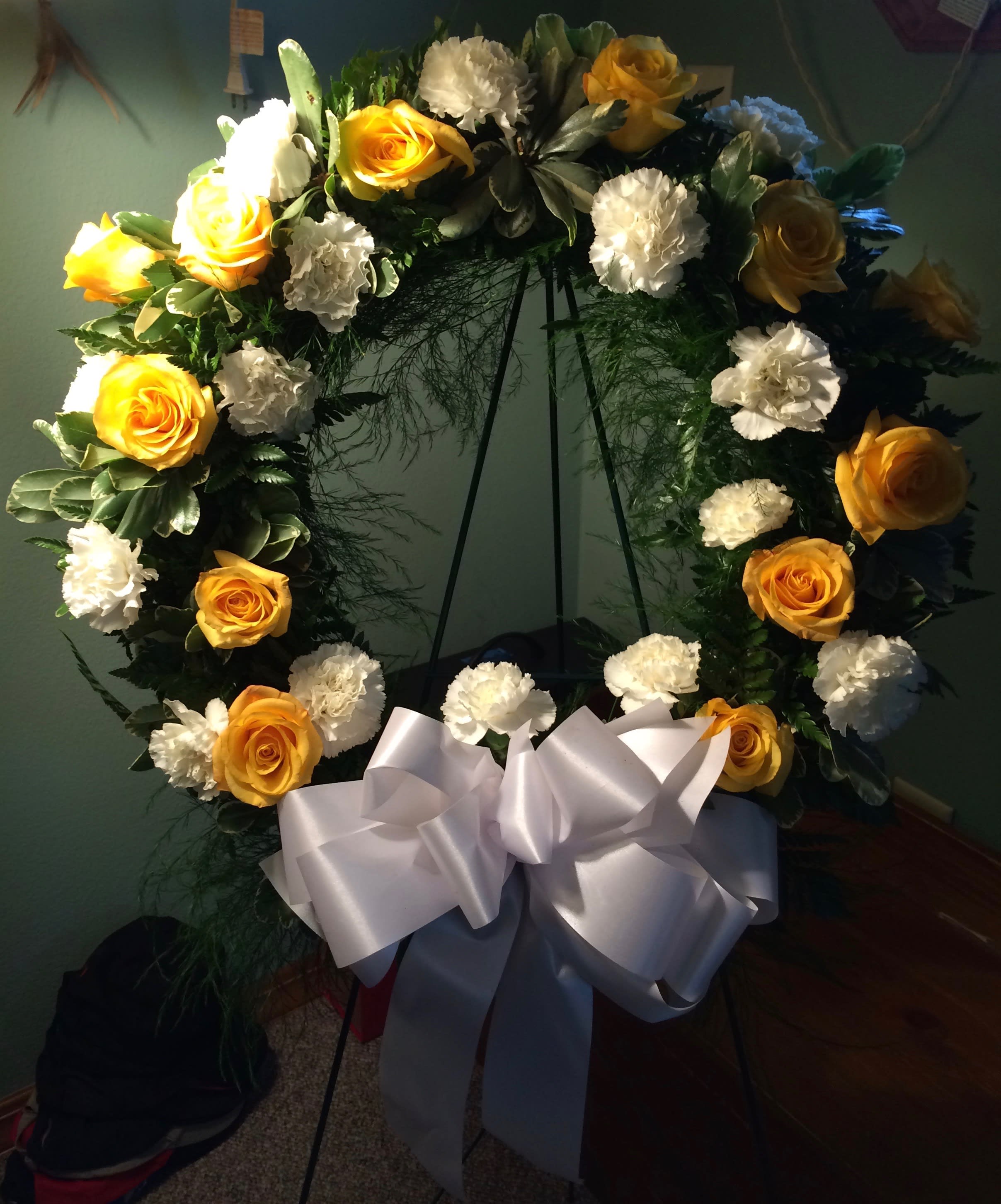 Yellow roses and white carnations arranged in a wreath with a white bow
