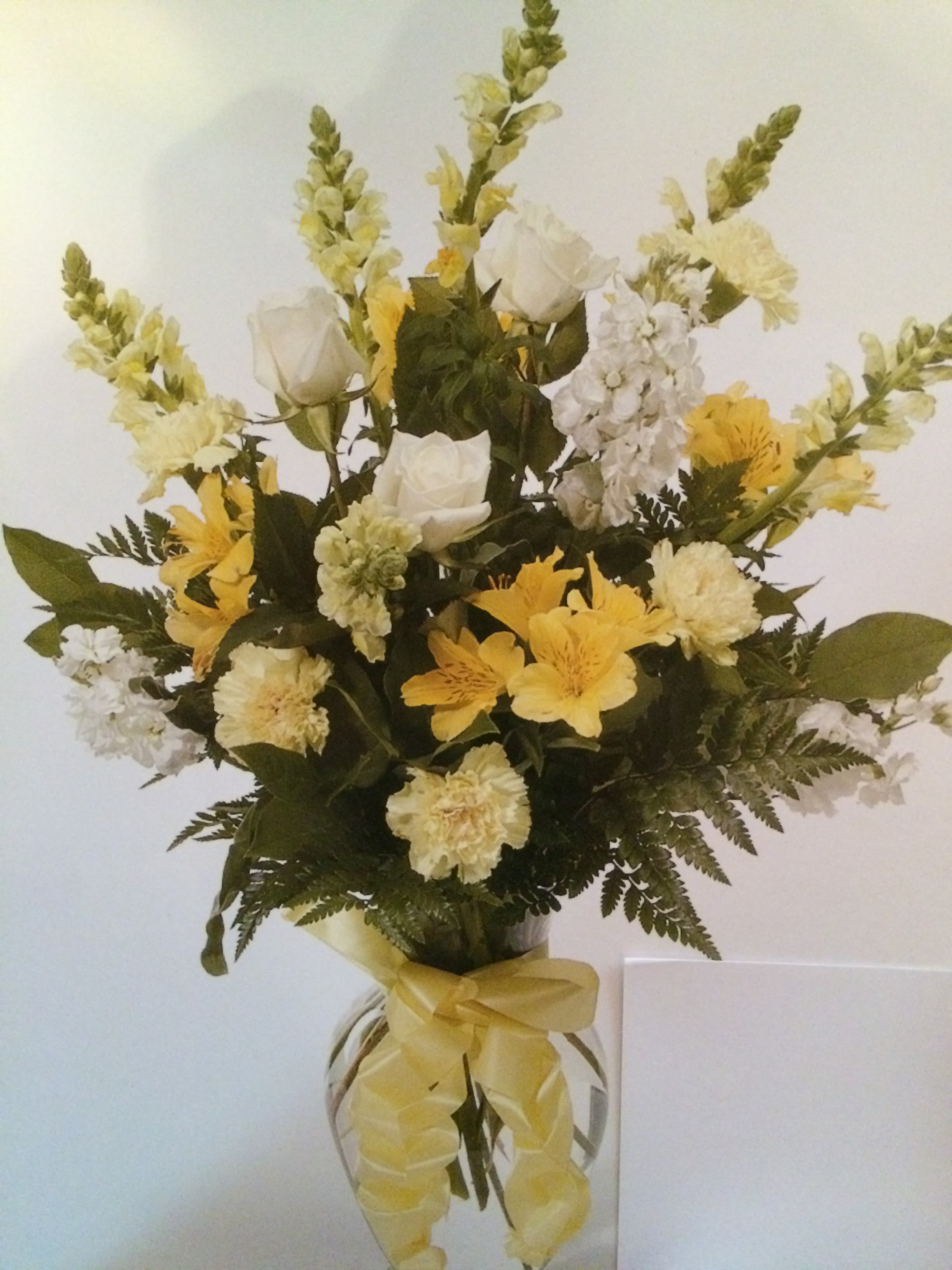 Yellow and white floral arrangement in a clear glass vase with a ribbon