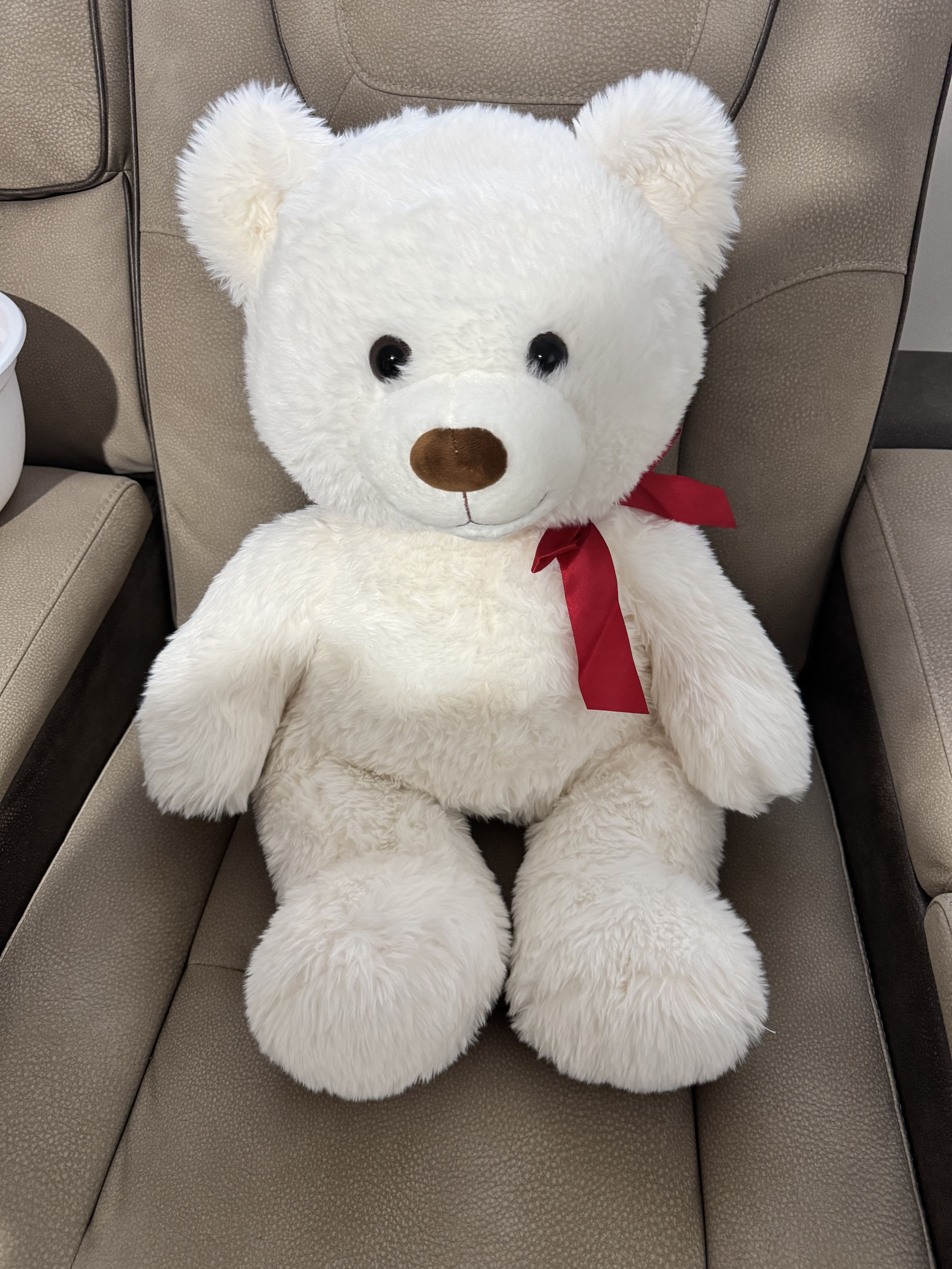 White teddy bear with a red ribbon sitting on a chair