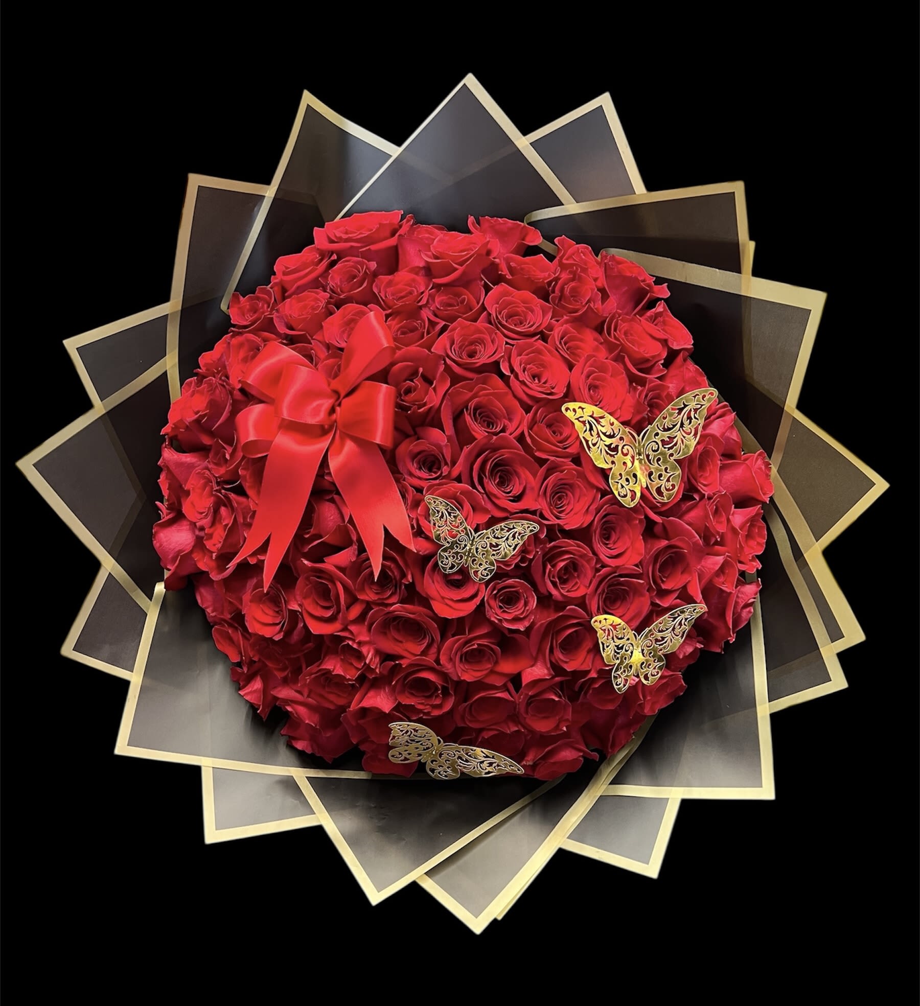 Round bouquet of red roses with red bow and gold butterfly accents in black and gold wrap
