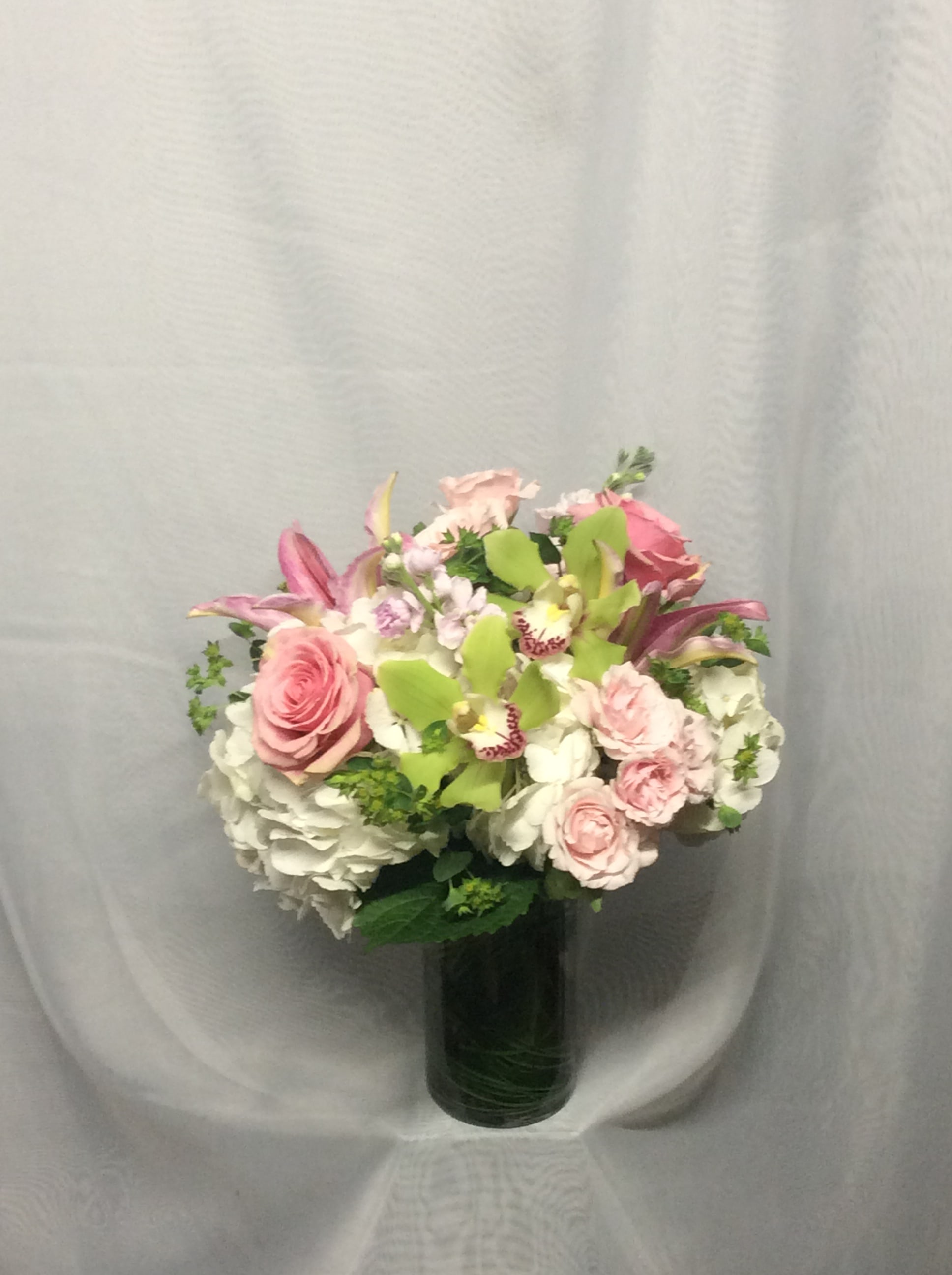 Round arrangement of pink roses, green orchids, and white hydrangeas in a clear glass vase