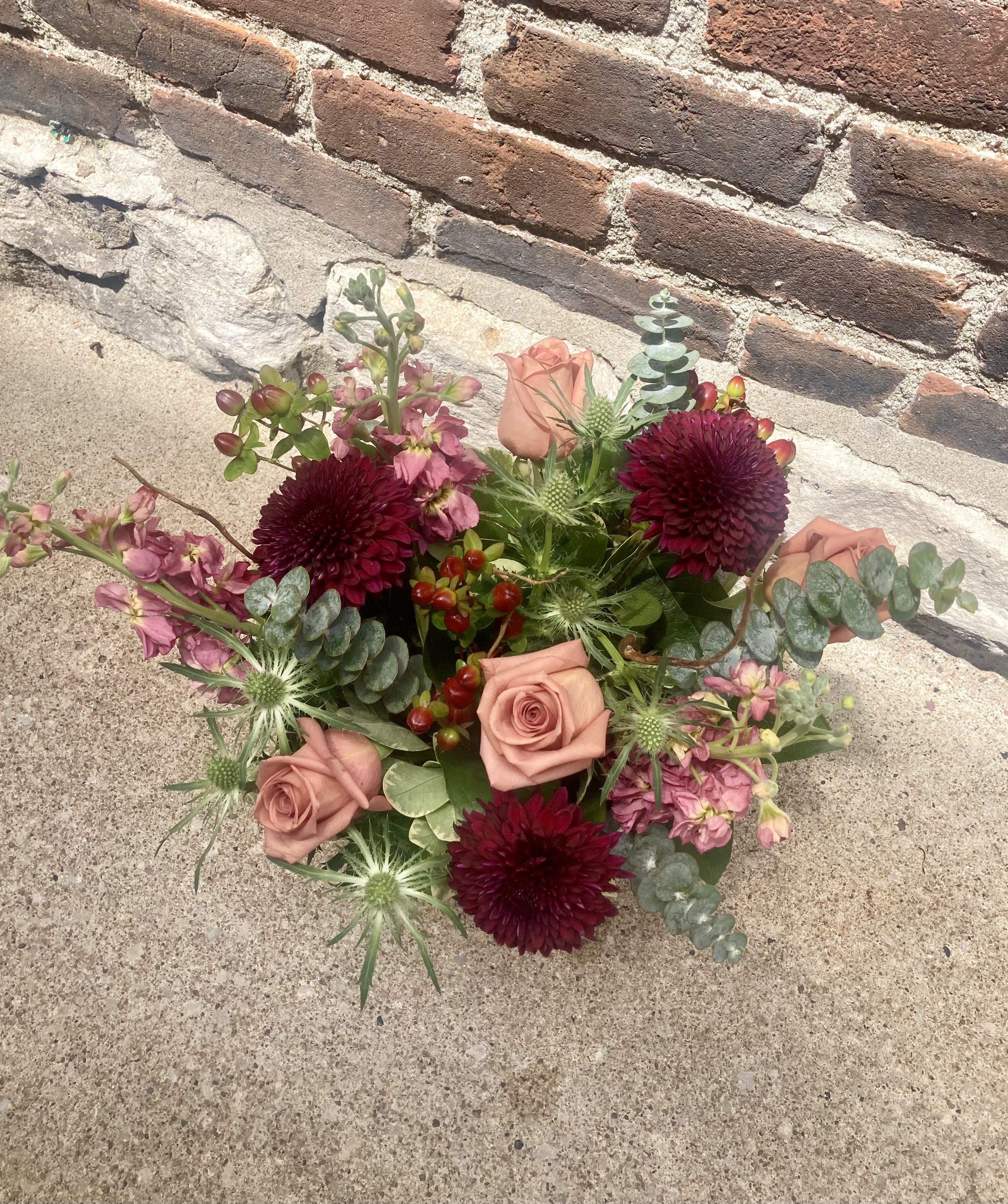 Blackberry Boho - Toffee colored roses paired with deep burgundy chrysanthemums give this flower arrangement a romantic, slightly moody look that still feels fresh and garden-made - ideal as a birthday bouquet, anniversary gift, or a thoughtful "just because" surprise. Presented in a clear glass vase, Blackberry Boho reads as an everyday mixed bouquet perfect for occasions from Mother's Day and Father's Day to Thanksgiving, Christmas, or a warm housewarming welcome.  The design layers soft stock and airy pink filler blooms around fuller roses and chrysanthemum heads, with spiky eryngium-like accents and rounded eucalyptus for texture and movement. Colors move from soft peach and pink through rich wine tones to cool green foliage for a lush, modern palette. Compact and slightly wild in silhouette, it fits on a desk or dining table and brings a lively, scented touch to any room.  Send Blackberry Boho to celebrate graduations, say thank you, offer sympathy, or brighten a get-well day - the recipient will feel seen and comforted by its thoughtful mix. Arrives arranged in a clear glass vase; for best care, refresh water every other day and trim stems slightly to extend vase life.