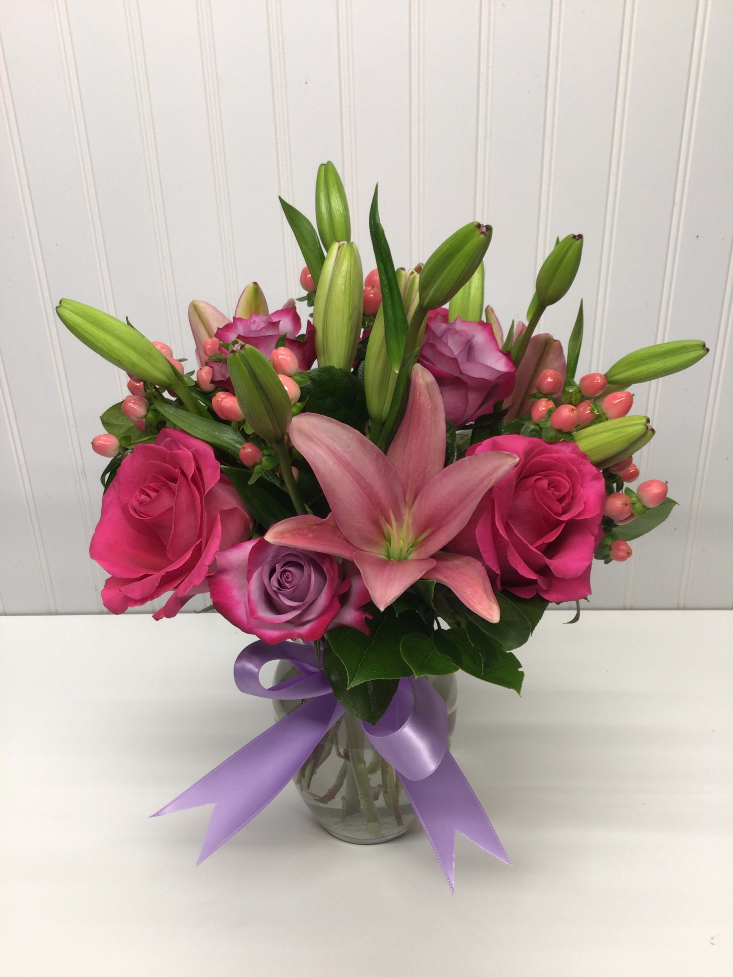 Pink lilies and roses with lavender roses in a glass vase tied with a lavender ribbon