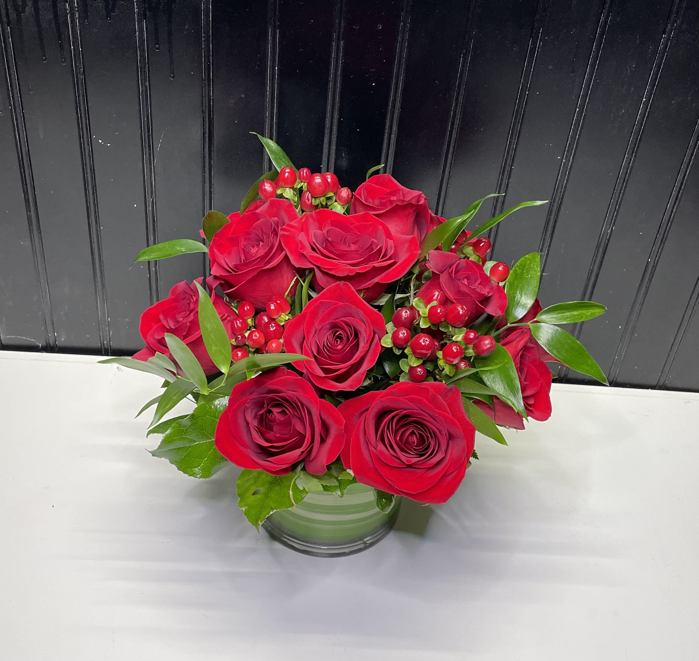 Red roses arranged in a clear glass vase with red berries