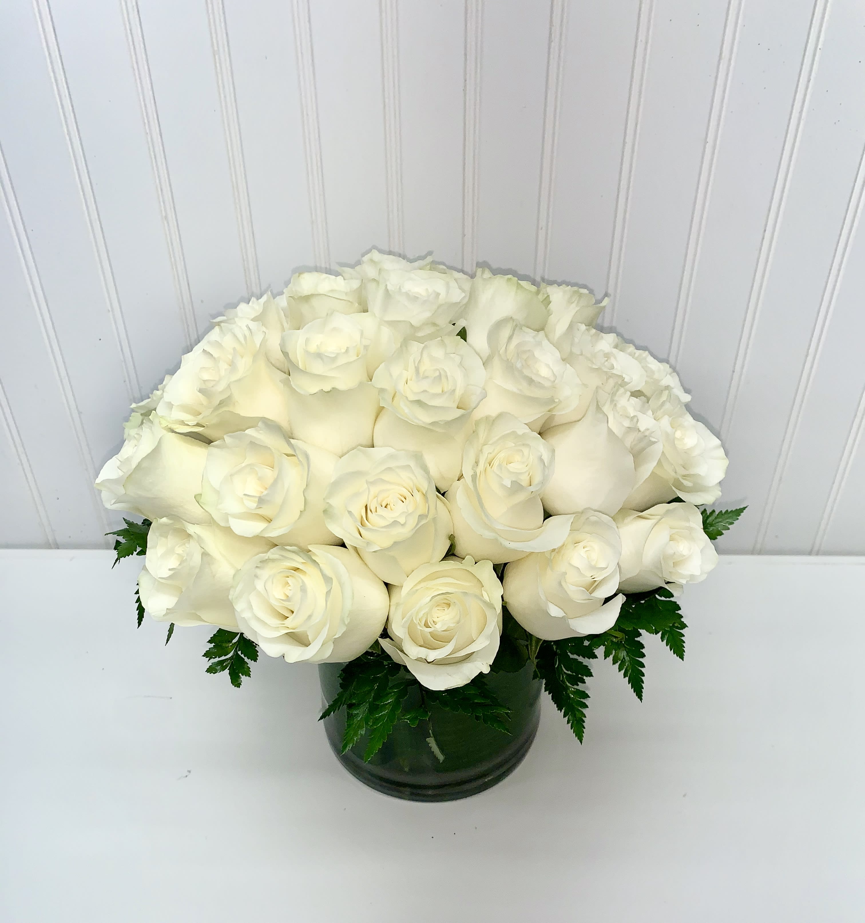 Low round arrangement of creamy white roses clustered in a clear glass cylinder vase