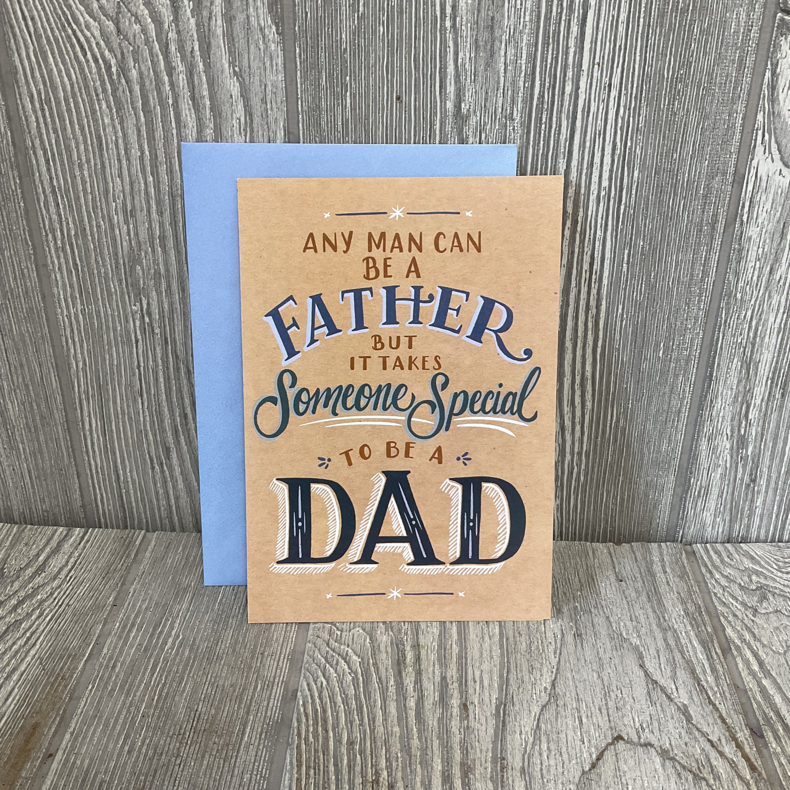 It Takes Someone Special To Be A Dad - Full Size Greeting Card - A warm, rustic Father's Day greeting card that says "It Takes Someone Special To Be A Dad"-perfect as a thoughtful add-on to a birthday, Father's Day bouquet, or a simple thank-you gift. The card's kraft-paper look and bold decorative lettering in blues and brown read as genuine and handmade, while the light blue envelope gives the whole package a soft, cheerful pop that will make the recipient feel seen and appreciated.  The folded card features a rustic brown cover with a printed Father's Day message and clean, sentimental typography that pairs well with casual, family-focused gifts. Sized as a full greeting card, it arrives with a matching light blue envelope and is ready to write in; use it to add a personal note to floral arrangements or gift bundles without extra wrapping.