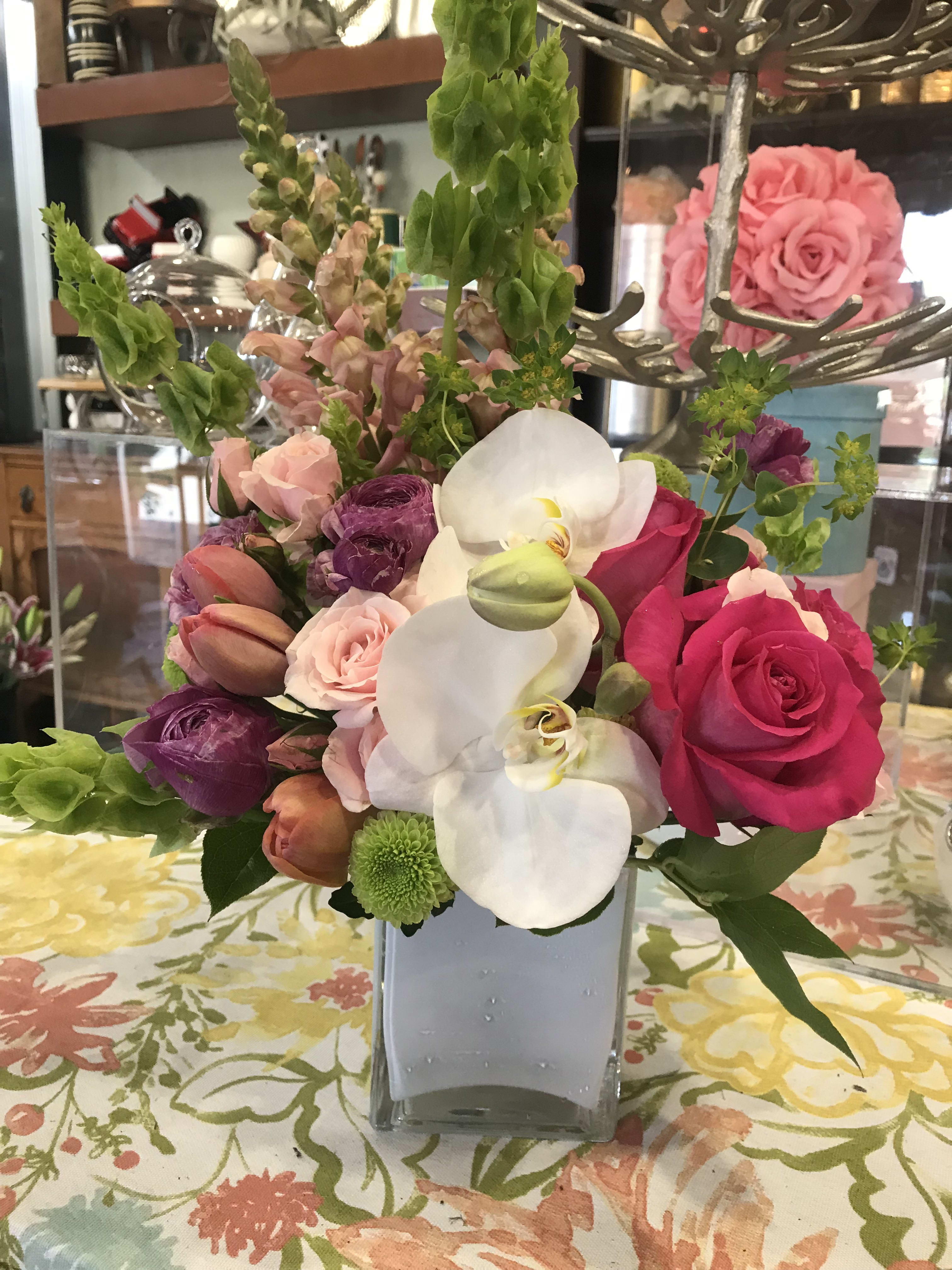 Mixed bouquet of pink roses, white orchids, and purple blooms in a square vase
