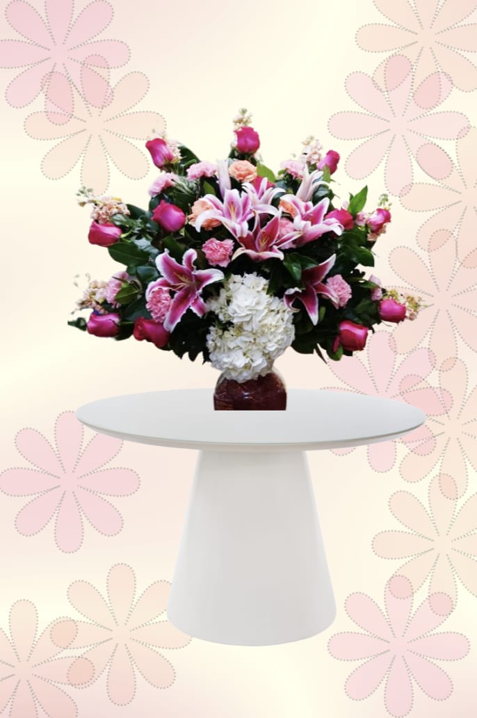 Lily Pink Dreams - Soft pink lilies and roses take center stage in this romantic flower arrangement-perfect as a birthday bouquet, Mother's Day gift, or anniversary surprise. Lily Pink Dreams presents a full, rounded design that reads feminine and celebratory; the recipient will feel cherished the moment they see the lush spray of blooms contrasted against deep green foliage.  Densely packed clusters of white hydrangea and pink carnations build texture and volume around the lilies and roses, creating a layered, garden-fresh look. The arrangement sits in a dark glass vase that sharpens the bright pinks and whites while adding elegant contrast; overall colors are pink, white, and green for a soft springtime palette that flatters any room or pedestal table display.  Choose this arrangement when you want someone to feel truly seen-whether marking an important milestone or simply saying "I'm thinking of you." The compact, rounded silhouette is easy to place on a mantel, bedside table, or dining pedestal; like fresh-cut flowers, keep stems trimmed and change the water every few days to extend the display.