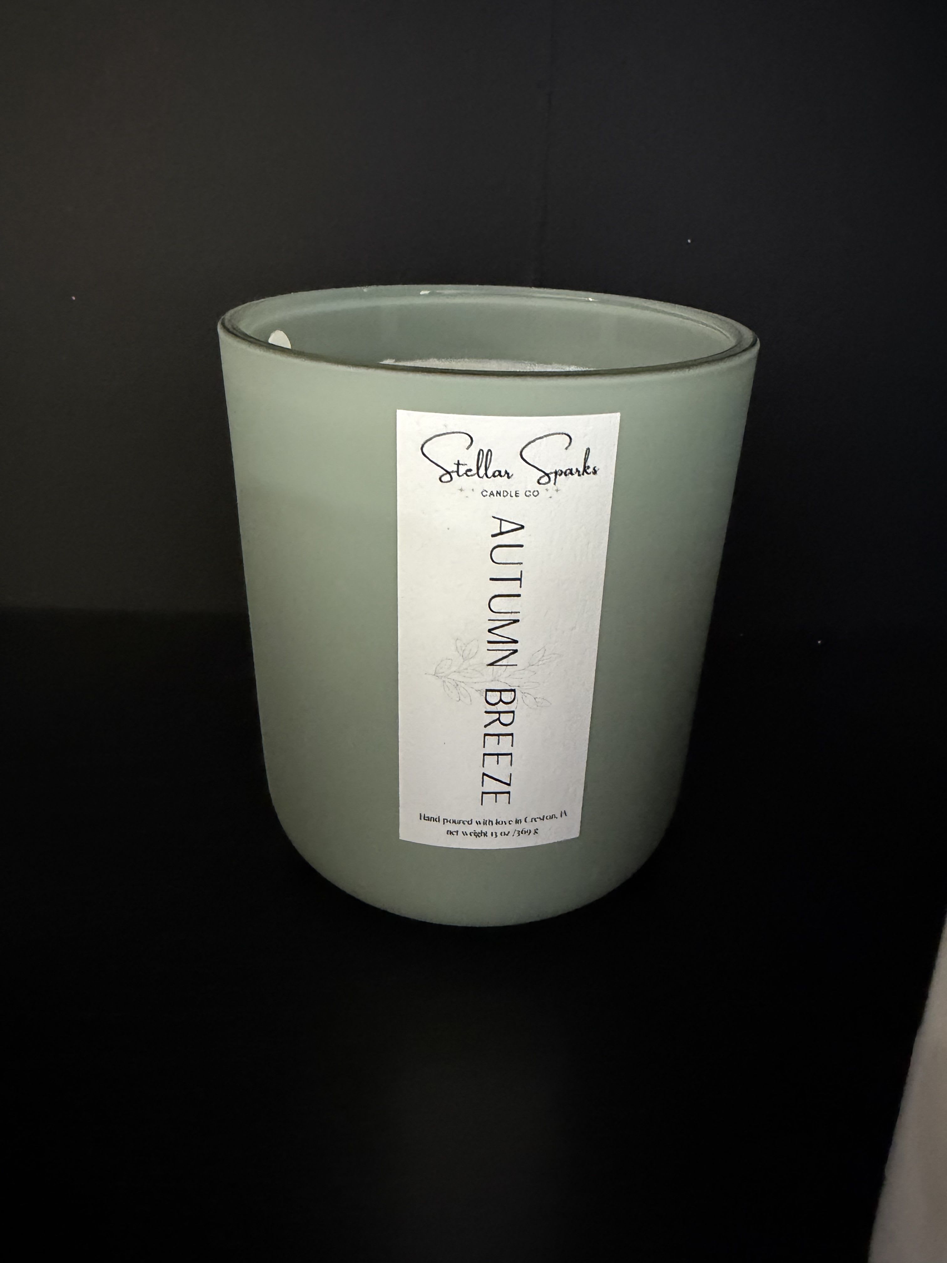 Autumn Breeze 13oz Candle - Muted sage green glass and a soft seasonal name set the tone: this Autumn Breeze 13oz candle is a calm, modern home fragrance gift that reads like a breath of late-season air. As a gift for someone who loves cozy evenings or for marking a small autumn moment, it's the kind of present that helps the person you're thinking of feel soothed and seen-perfect for a birthday, hostess gift, or a thoughtful "thinking of you" moment.  The candle arrives in a 13oz muted sage glass jar with a tall white label stamped "Autumn Breeze," giving it a clean, minimal look that complements green, white, and black decor. Housed in a simple glass candle jar with a tasteful label, it presents as an understated accent rather than a floral arrangement-ideal on a coffee table or bedside. Care: burn on a heat-resistant surface, trim wick to 1/4" before lighting, and let the melt pool reach the jar edge on first burn for an even fragrance throw.