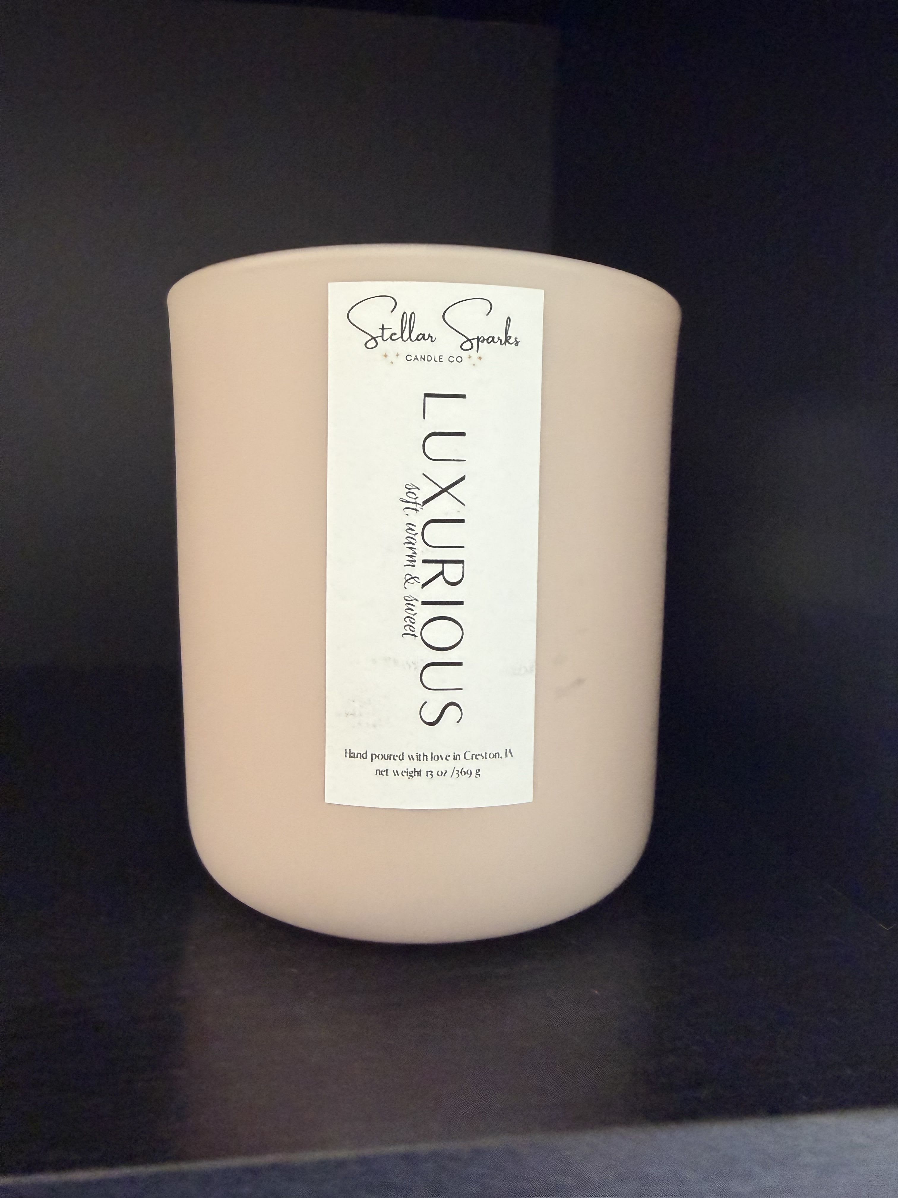 Luxurious 13oz Candle - A calm, understated gift that reads like a quiet moment at home - this flower-arrangement-adjacent product pairs beautifully with sympathy bouquets or a "thinking of you" gift. As a floral-friendly home accessory for occasion-driven orders such as sympathy arrangements, hostess gifts, or get-well gestures, the candle's neutral palette and soft scent help your person feel soothed and seen.  The 13 oz glass jar candle comes in a rounded beige container with a tall white front label reading "Luxurious" by Stellar Sparks Candle Co., and offers a soft, warm, sweet fragrance that complements white and neutral flower arrangements without overpowering them. The simple glass jar and elegant label make it easy to add to an arrangement or include as a standalone present; its size is substantial enough to provide hours of scent and atmosphere, and the clean styling fits a range of home décors.