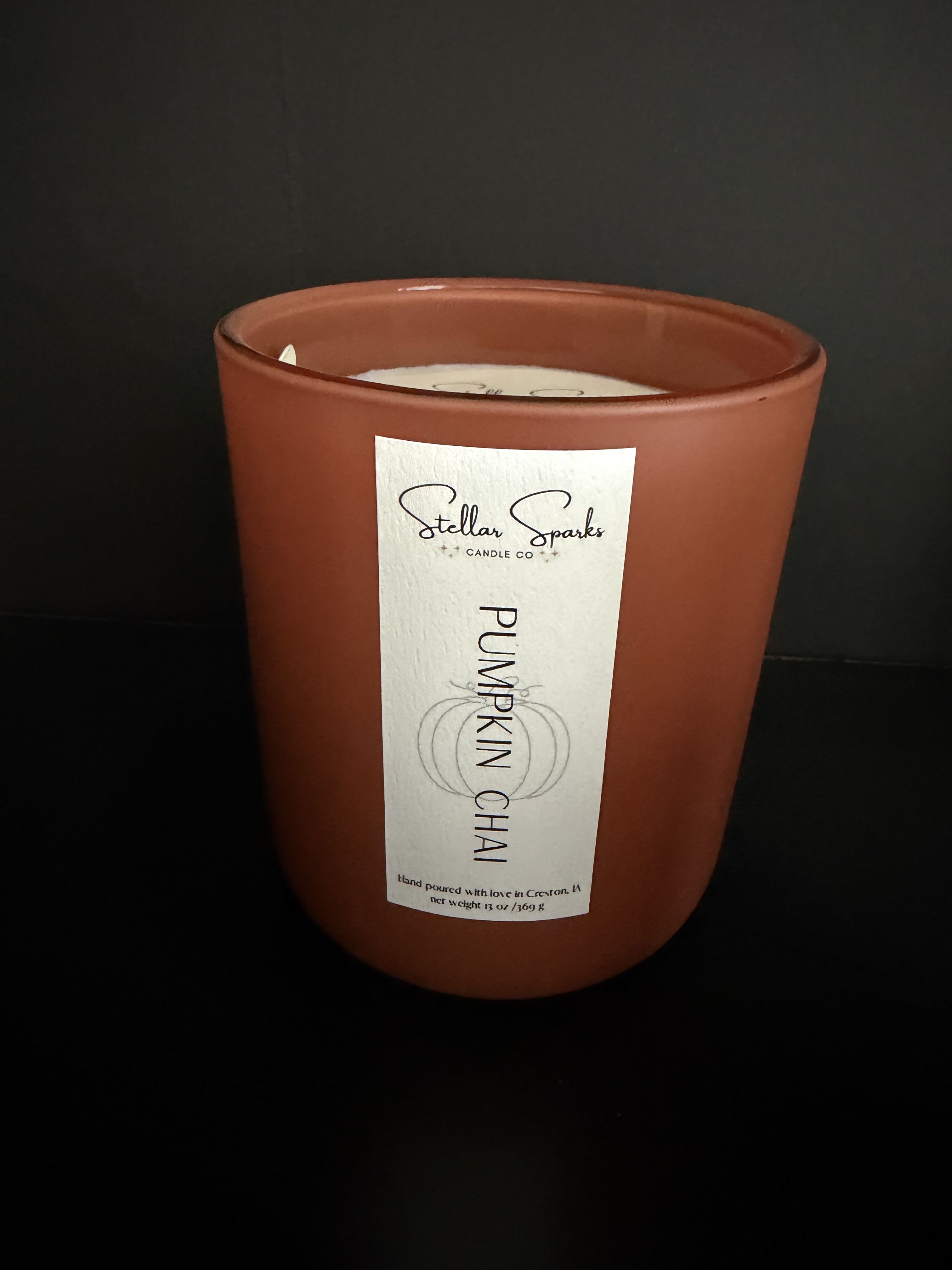 Pumpkin Chai 13oz Candle - A warm, cozy accent for autumn gifting: this 13oz Pumpkin Chai candle is a seasonal home fragrance perfect as a fall gift, hostess present, or small Thanksgiving surprise. The candle's matte brown glass jar and simple white label read as quietly sophisticated-she'll feel wrapped in a comforting, spicy moment when the scent fills the room, making it ideal for anyone who loves cozy evenings and pumpkin-scented warmth.  The candle comes in a 13oz terracotta‑tone matte glass jar with a centered white label that reads "Pumpkin Chai," offering an elegant, minimalist look that pairs beautifully with orange, white, and black fall decor. Presented as a single jar with its label intact, it's sized for tabletop or mantel display and designed to blend with seasonal florals or a curated gift box.  Choose this candle to mark autumn birthdays, host/hostess thanks, or simply to say "thinking of you" during cooler months-the scent and muted color palette make the recipient feel comforted and seen. Burn in a well‑ventilated area and place on a heat‑resistant surface; the 13oz size provides several hours of fragrance, making it a thoughtful standalone gift or a complement to a bouquet.