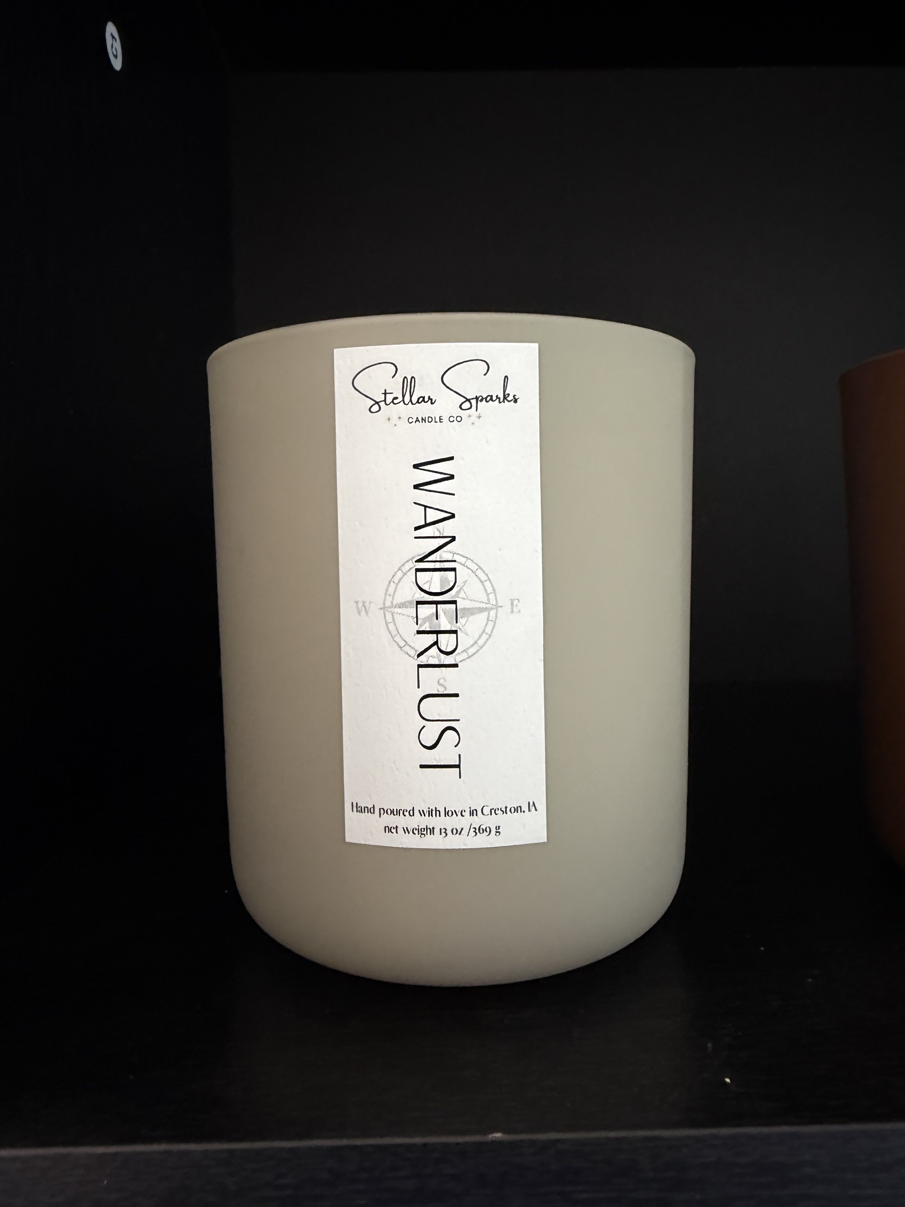 Wanderlust 13oz Candle - A calming, minimalist scent that feels like a quiet room on a weekend morning-this 13oz candle is a perfect gift when you want to help someone unwind. As a home fragrance item for housewarming, thank-you, or just-because moments, the Wanderlust candle offers a neutral, soothing presence that will make the person you're thinking of feel cared for and quietly indulged.  The candle comes in a smooth glass jar with a tall white label reading "Wanderlust" and the Stellar Sparks Candle Co. name for a clean, modern look that fits any decor. The wax is a large beige tone paired with simple product labeling, and the package includes the glass candle jar and label as shown. Its understated palette-white and neutral-lets the candle blend into bedroom, living room, or office settings without overpowering the space.  Give this candle as a thoughtful accompaniment to a bouquet or on its own for birthdays, housewarmings, or moments when someone needs a little peaceful luxury. The 13oz size makes it substantial enough to enjoy over many evenings; place on a stable surface, trim the wick before each burn, and follow standard candle-safety practices when in use.