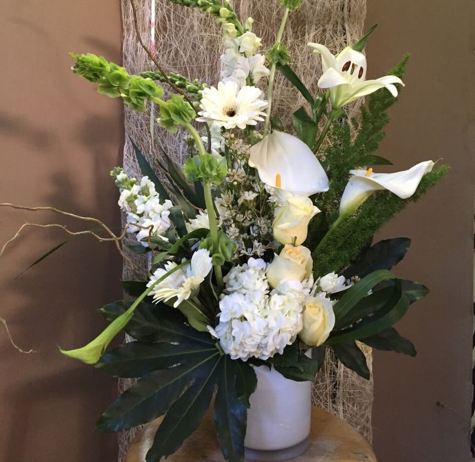 White floral arrangement with calla lilies, roses, and gerbera daisies in a white vase