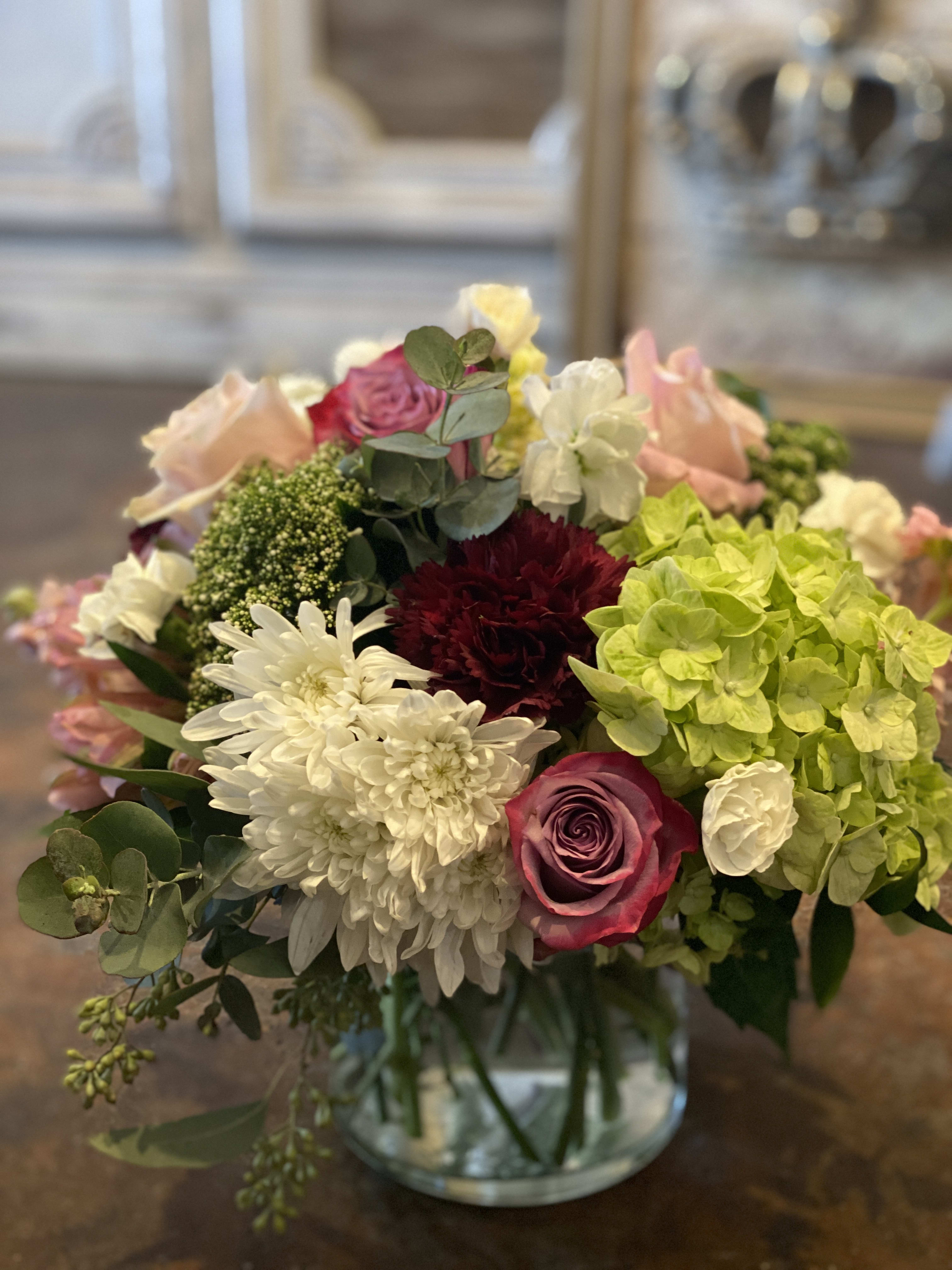 Mixed bouquet of roses, hydrangeas, and white chrysanthemums in a glass vase
