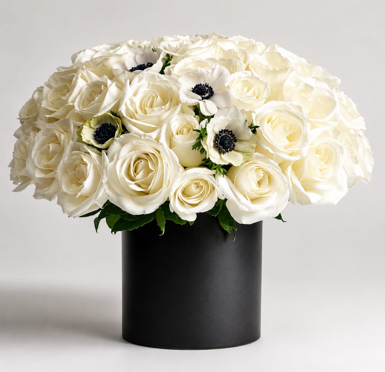 The Signature- Panda - As Shown. A perfect pairing of 36 white roses, anemone, and Israeli ruscus leaves make up this stunning piece! Perfect for any expression of love.