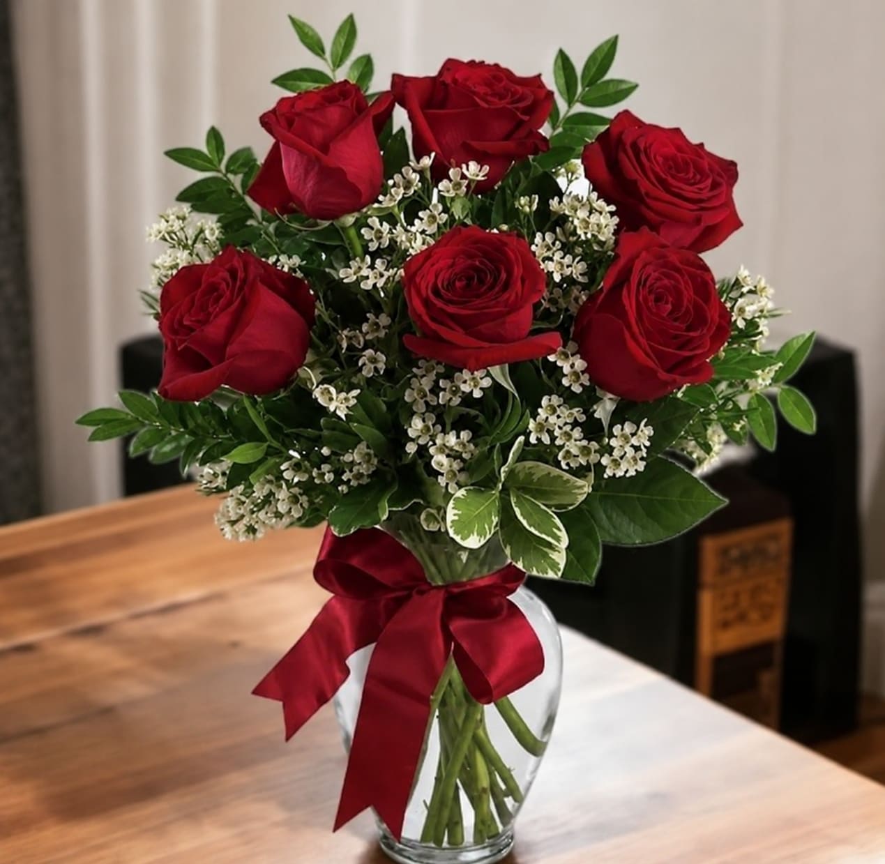 Romantic Roses - A timeless arrangement of premium red roses, delicate white wax flowers, and fresh greenery in a clear glass vase. Elegant, romantic, and perfect for celebrating love, appreciation, and life's special moments.