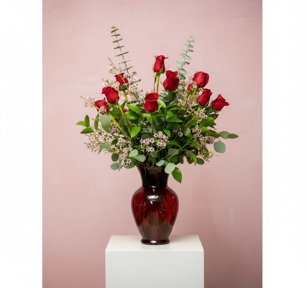 Red roses arranged in a dark glass vase with greenery