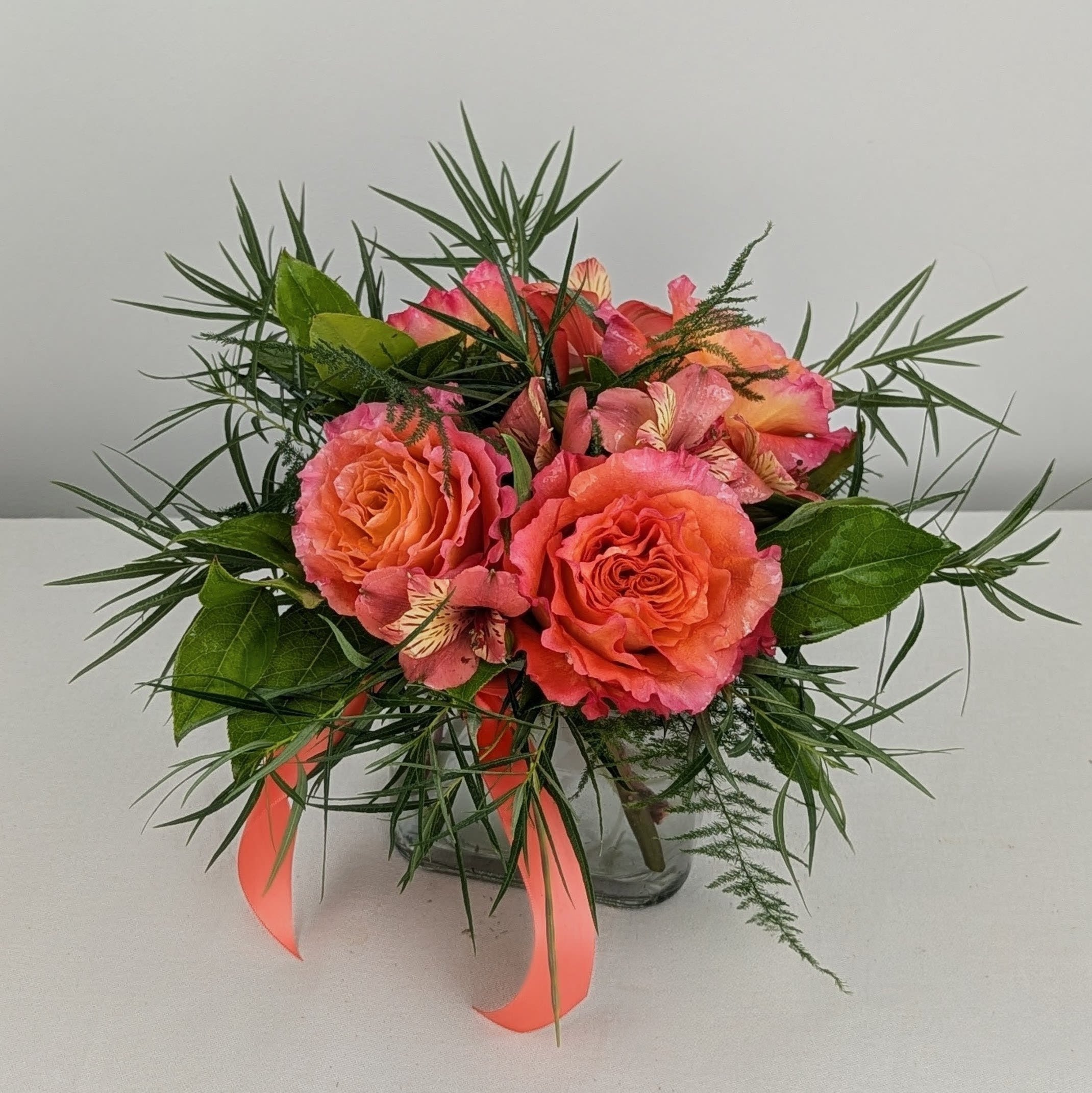 Coral roses and pink alstroemeria in a glass vase with ribbon