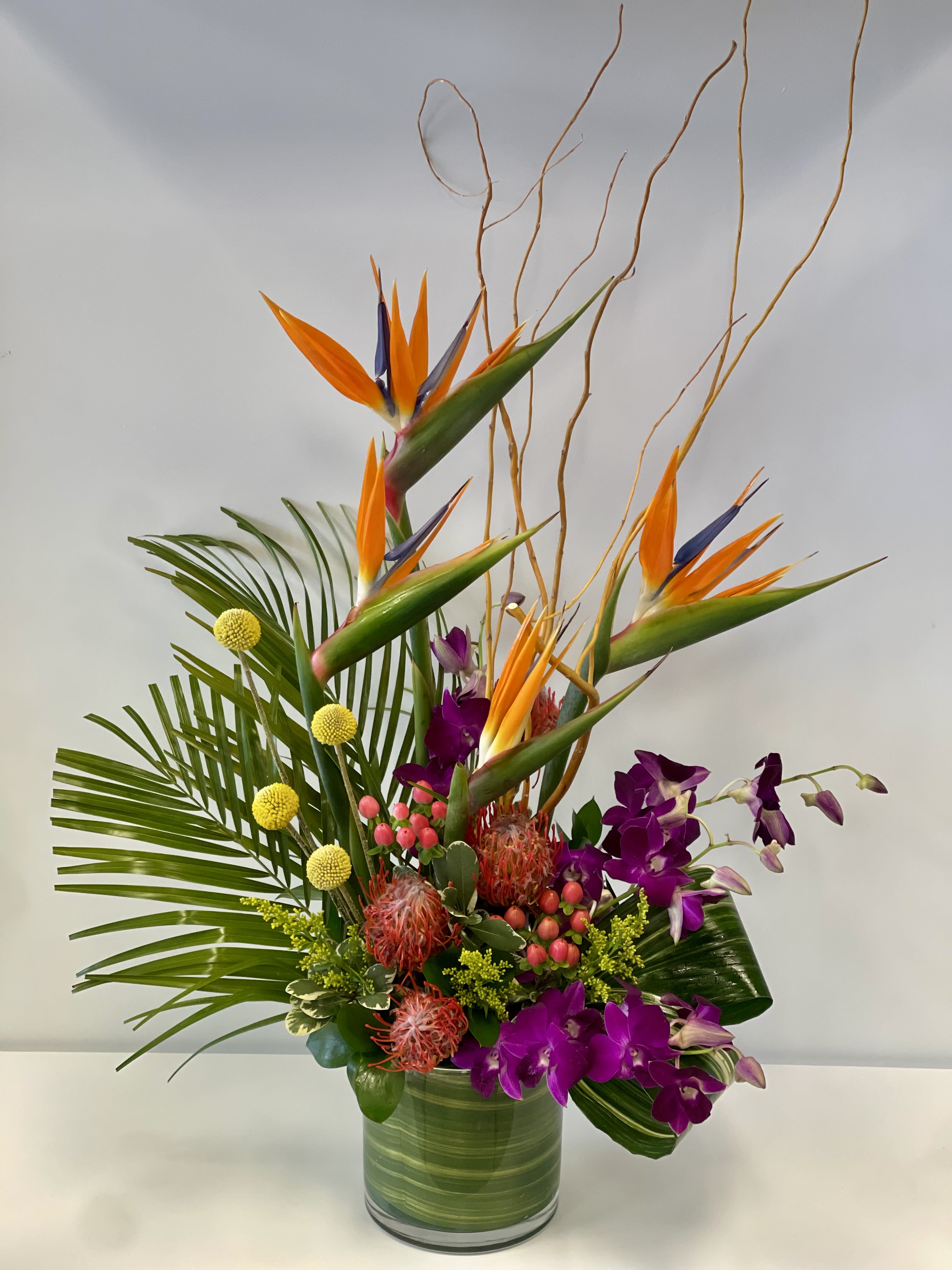 Tropical arrangement with orange bird of paradise and purple orchids in a glass vase