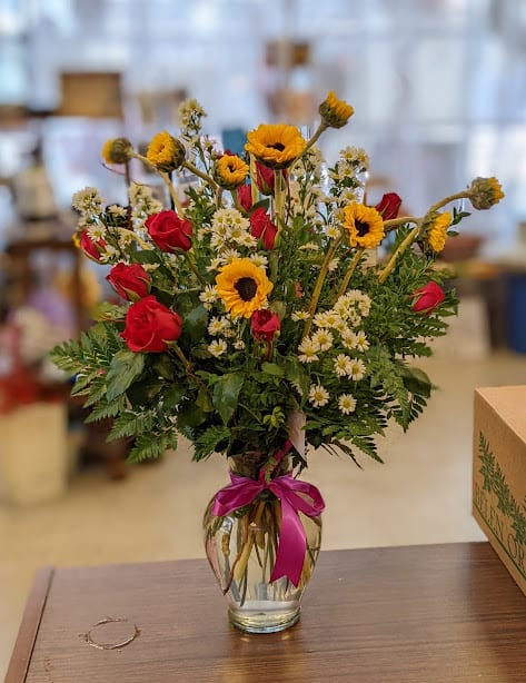 Bouquet of red roses and yellow flowers in a clear glass vase with a pink ribbon
