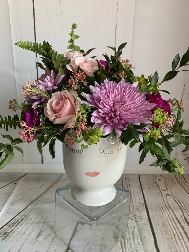 Pink and lavender flowers arranged in a white face vase