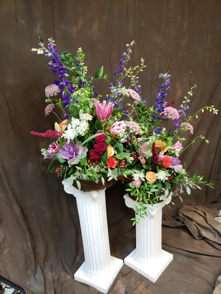 Two tall floral arrangements in white pedestal stands with pink, purple, and red blooms.
