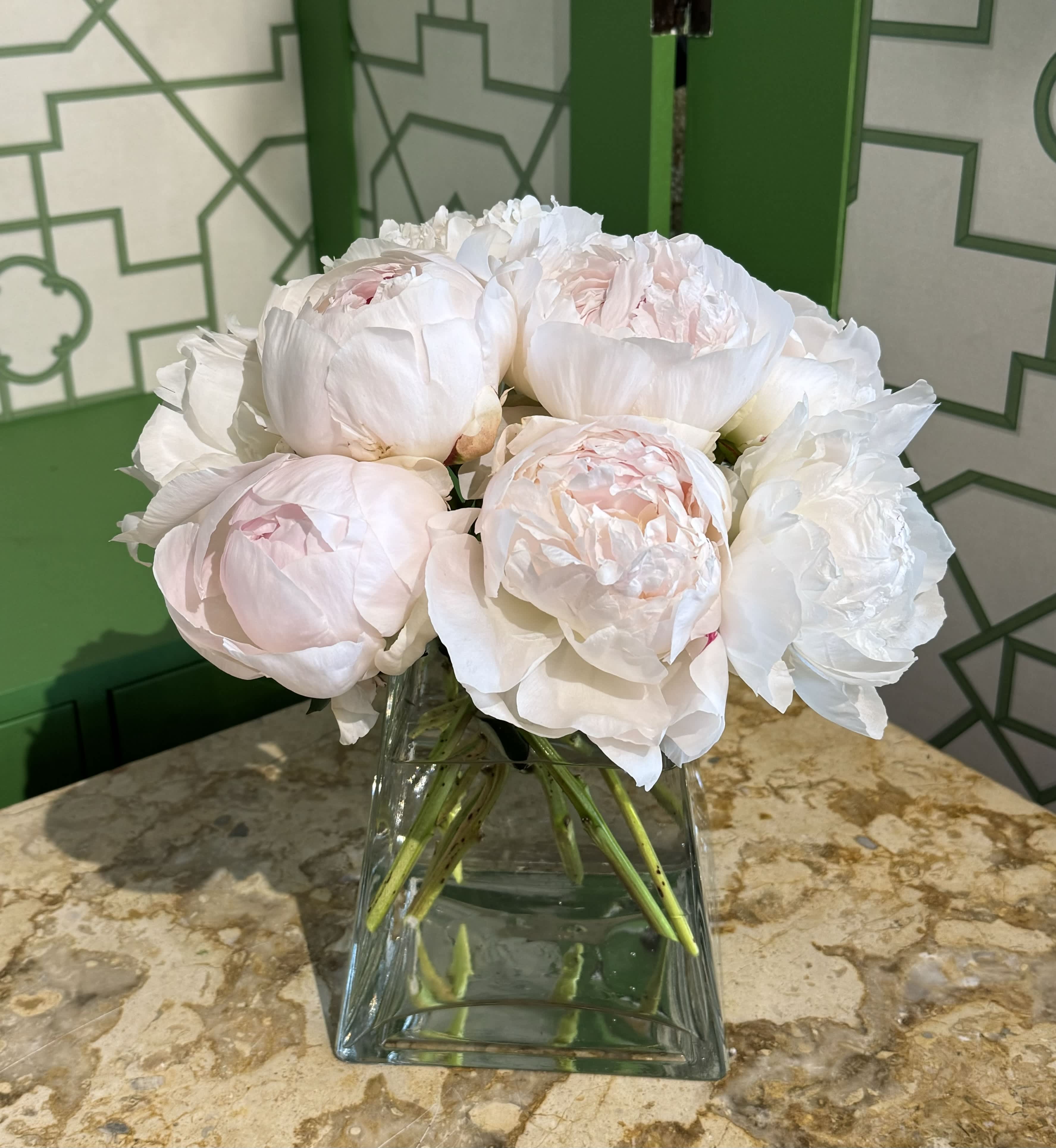White and pale pink peonies arranged in a clear glass vase