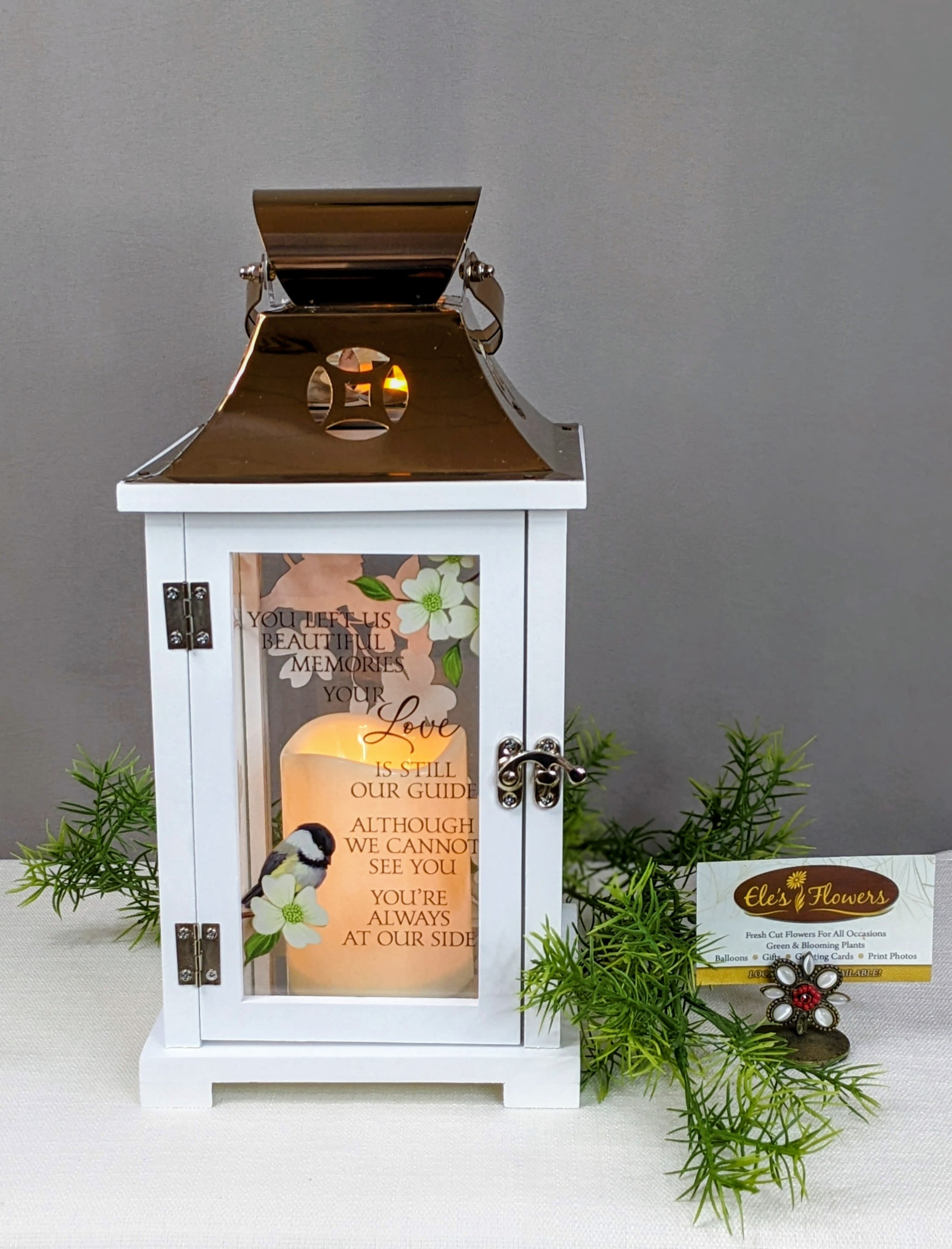 White memorial lantern with gold top and glowing candle, printed with verse and bird illustration.