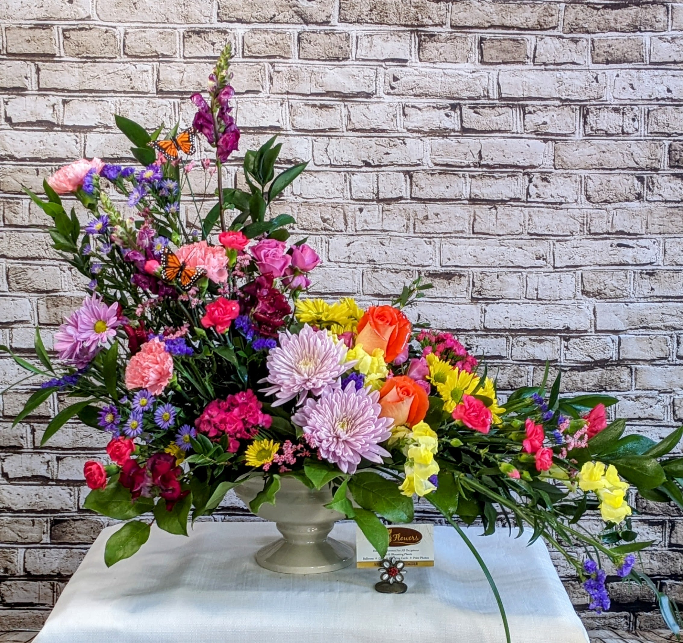 Colorful mixed flower arrangement in a pedestal vase with butterfly accents