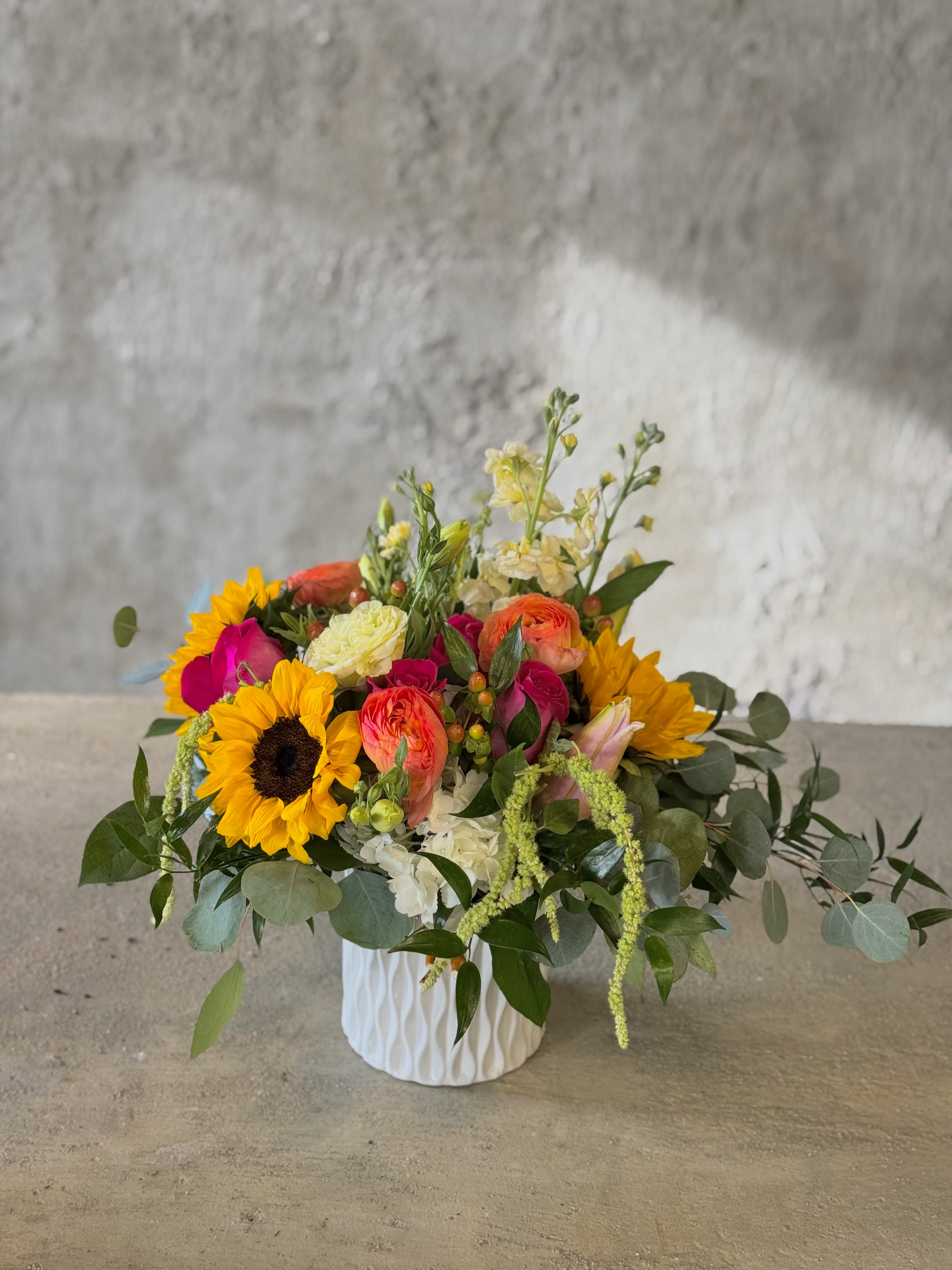 Mixed bouquet in a white textured vase with sunflowers and bright pink blooms