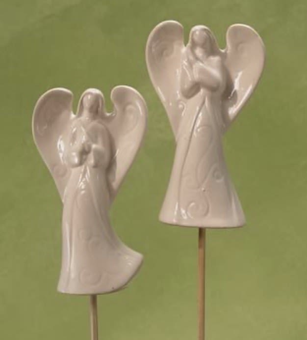 Two white ceramic angel ornaments on sticks against a green background
