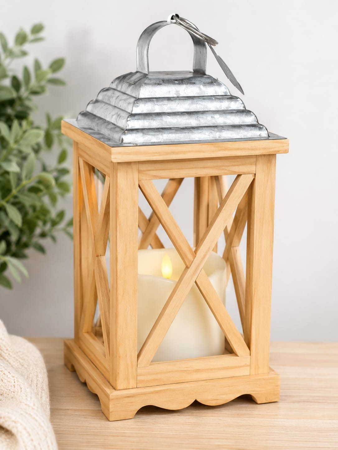Rustic Lantern - Rustic Wooden Lantern combines farmhouse charm and warm lighting in a versatile decorative accent. Featuring a natural wood frame, galvanized metal top, and battery-operated LED candle, this lantern adds a welcoming glow to homes, covered porches, gatherings, celebrations, and special events. The LED candle requires three AAA batteries and provides the look of candlelight without an open flame.  Its neutral design complements farmhouse, rustic, cottage, and traditional decorating styles. The Standard version includes the lantern, LED candle, and a complimentary coordinating ribbon. Our Deluxe version pairs the lantern with a coordinating fresh floral arrangement designed to enhance its natural character. The Premium version features the lantern surrounded by a fuller floral design with additional flowers, greenery, and texture.  Appropriate for housewarmings, thank-you gifts, retirement celebrations, weddings, holidays, sympathy occasions, and everyday decorating, the Rustic Wooden Lantern offers year-round appeal. Whether displayed indoors or on a covered porch, it provides a simple and timeless decorative touch. Beautiful, versatile, and easy to display, this lantern is designed to complement a variety of homes, occasions, and personal styles.