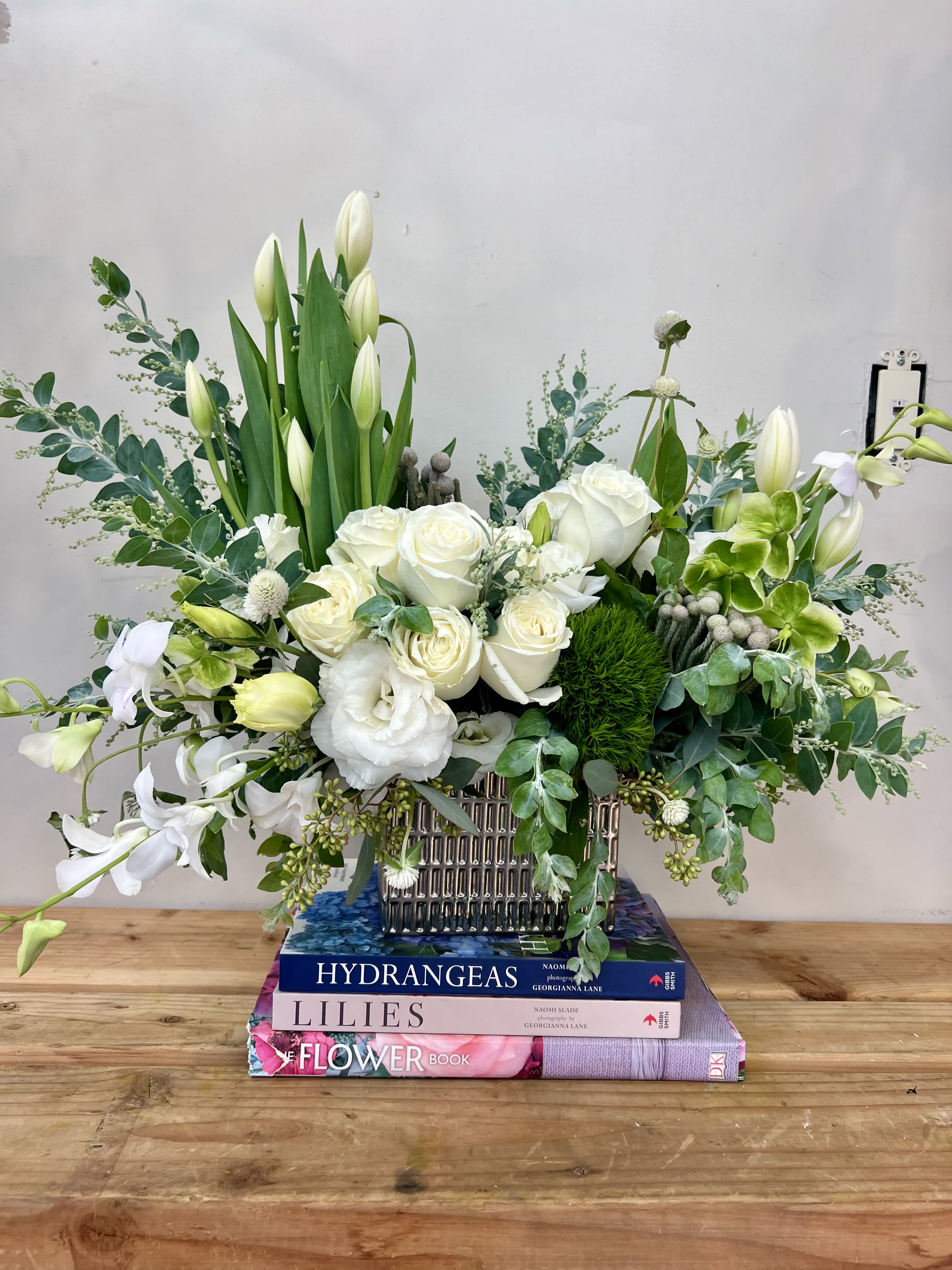 White roses and lilies arranged in a silver vase with green foliage