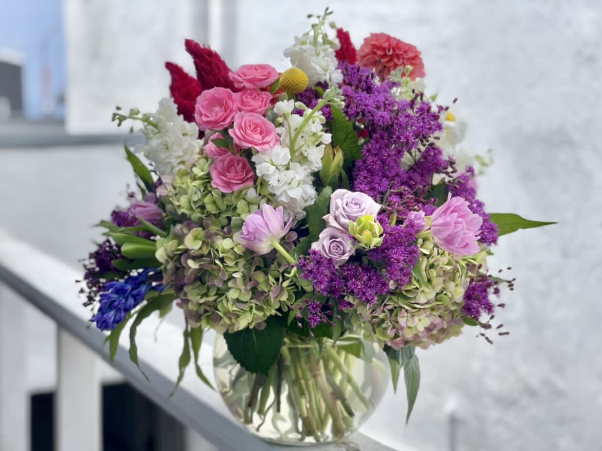 Mixed bouquet of pink, purple, white, and blue flowers in a clear glass vase