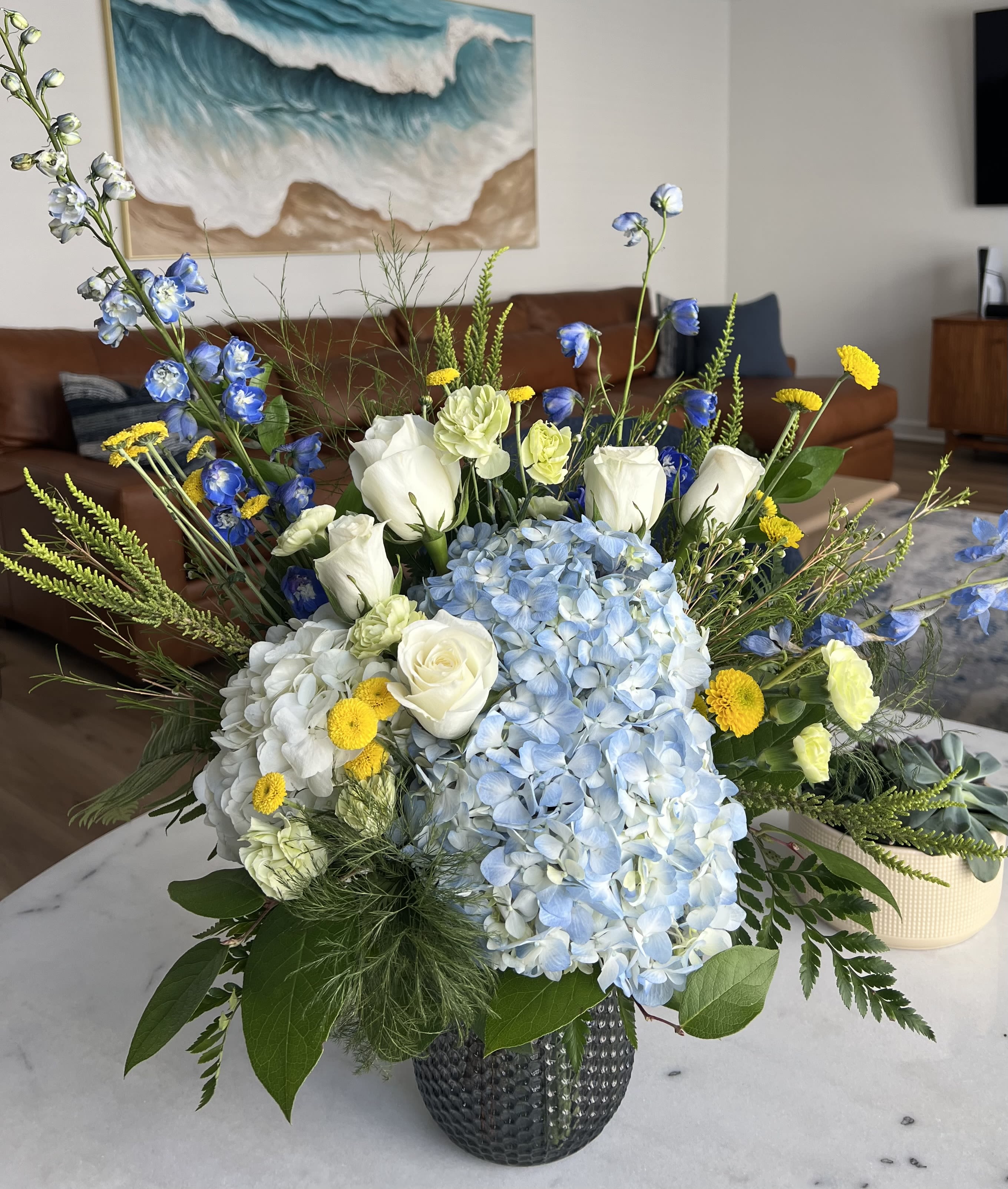 Blue and white floral arrangement with roses, hydrangeas, and yellow accents in a vase