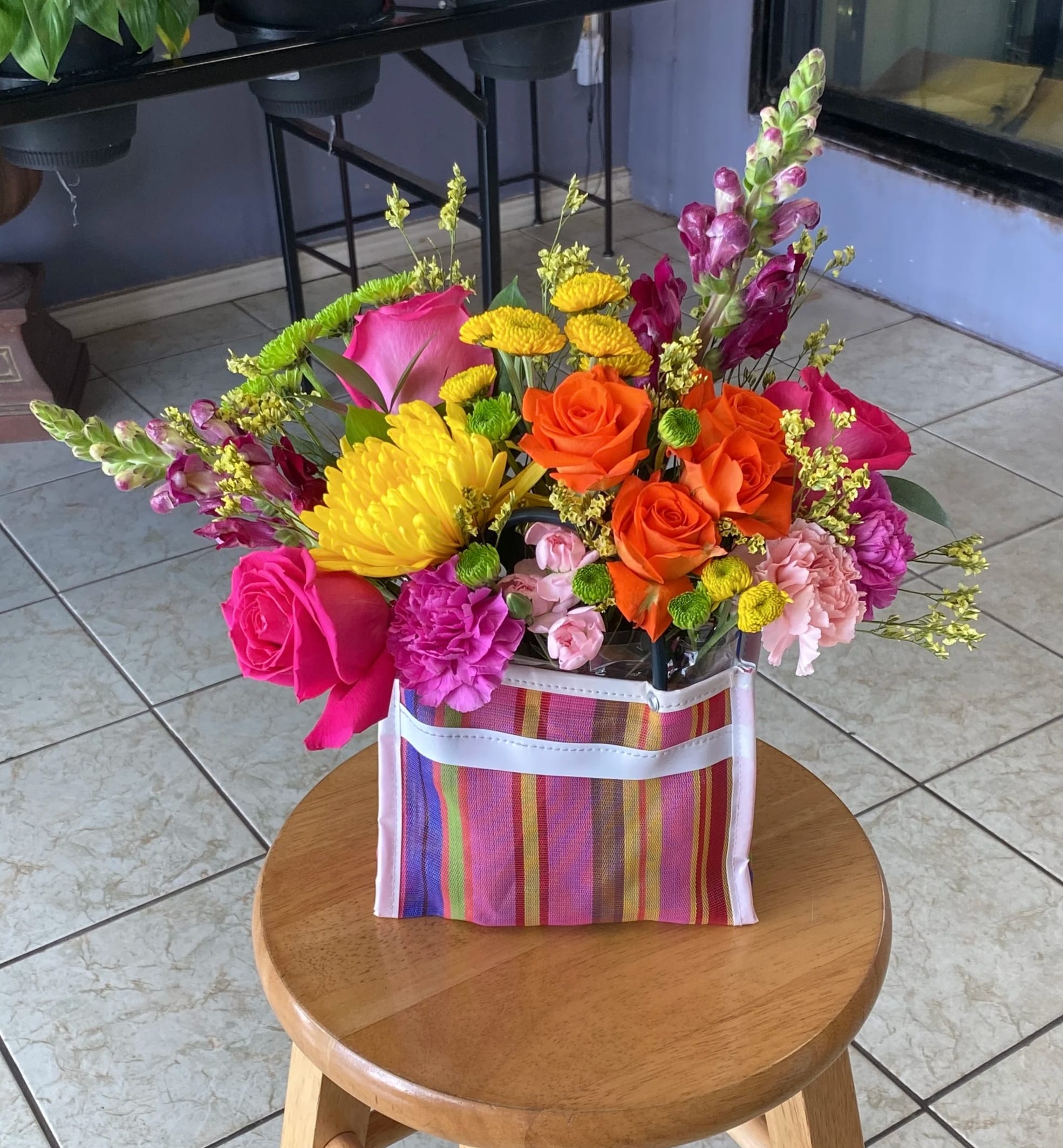 Bright mixed bouquet in a striped gift bag with roses, chrysanthemums, and snapdragons