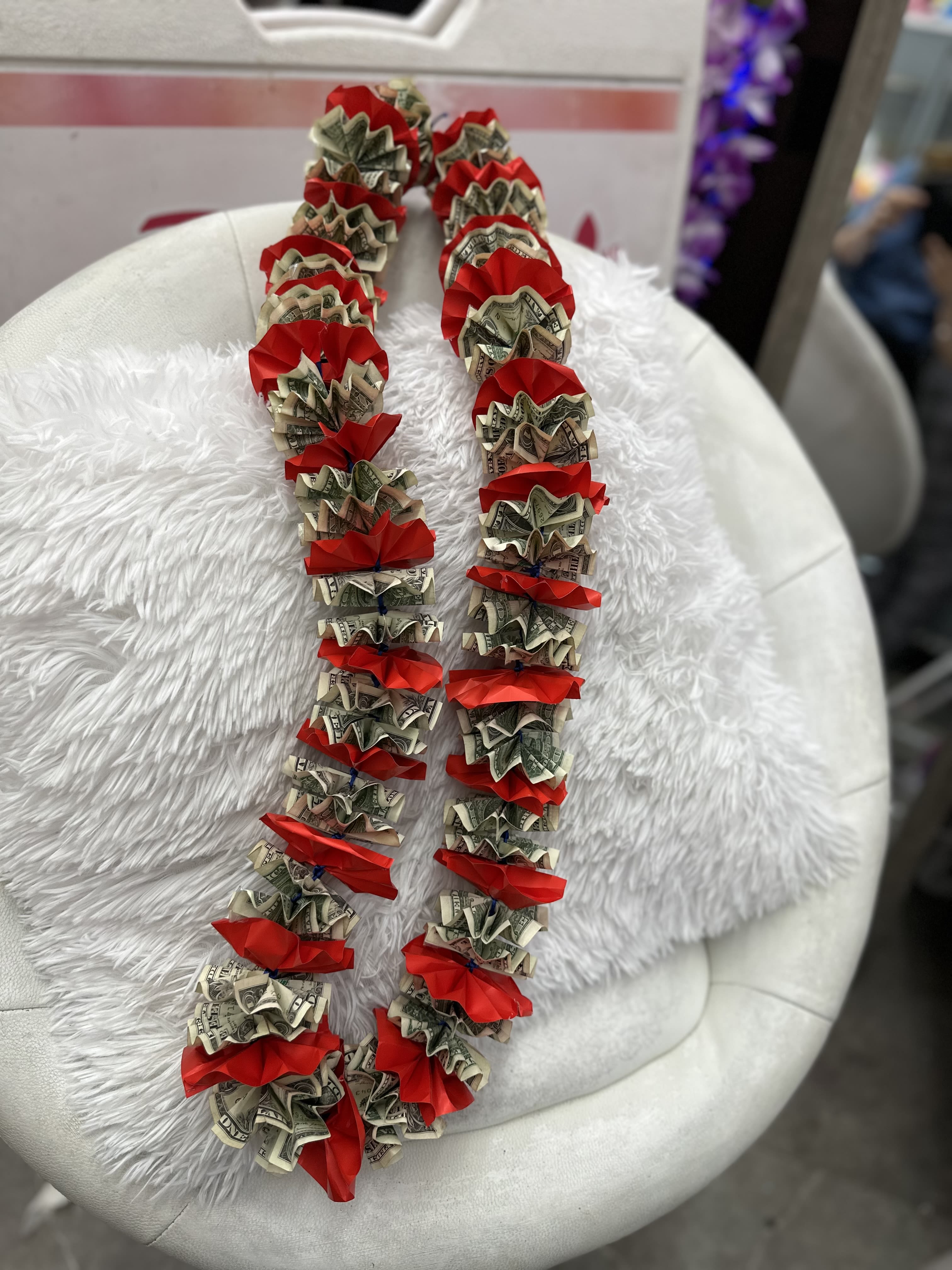 Money lei with red ribbon accents draped over a white chair