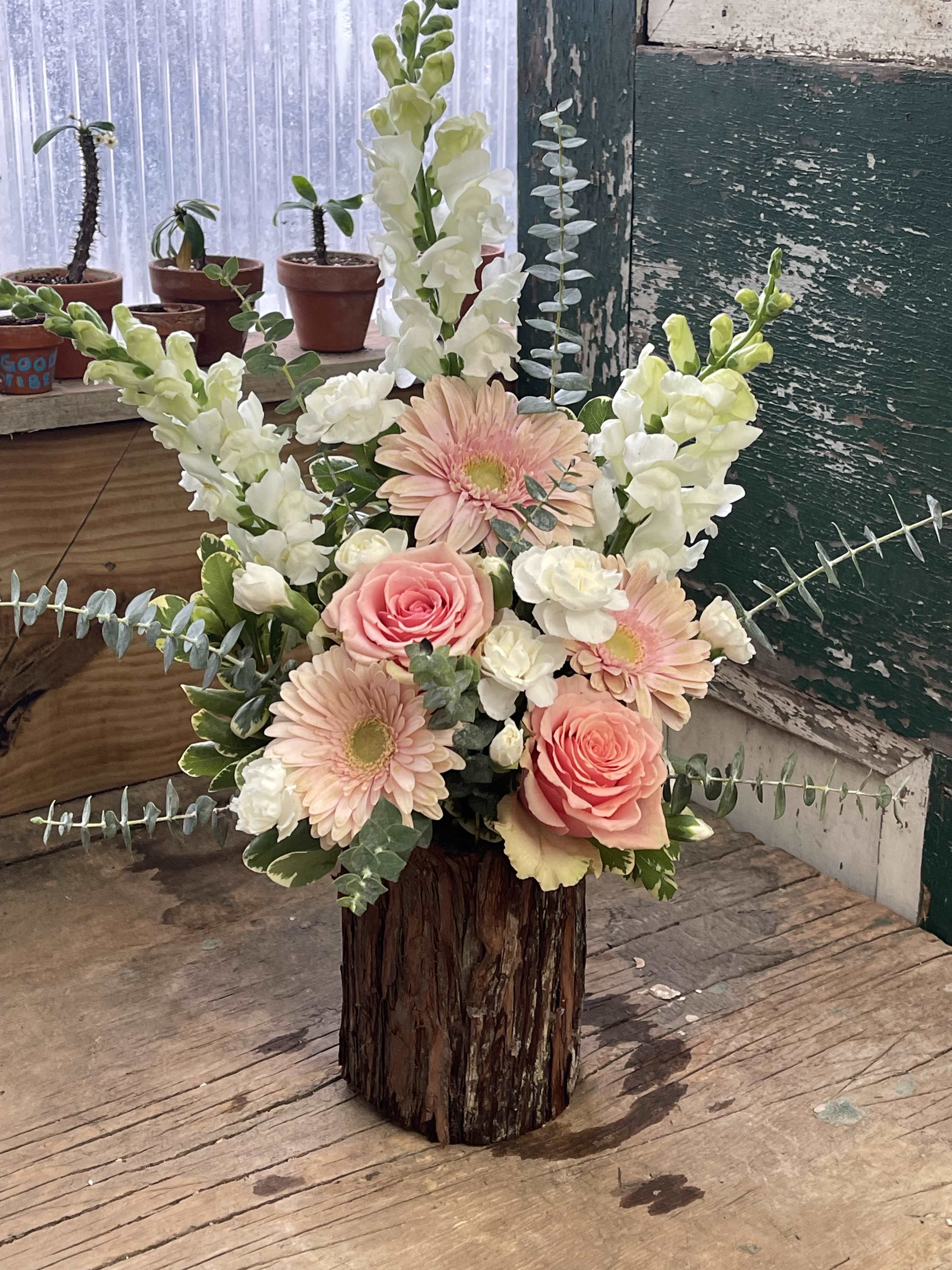 Pink roses and gerbera daisies in a rustic wood vase with white snapdragons