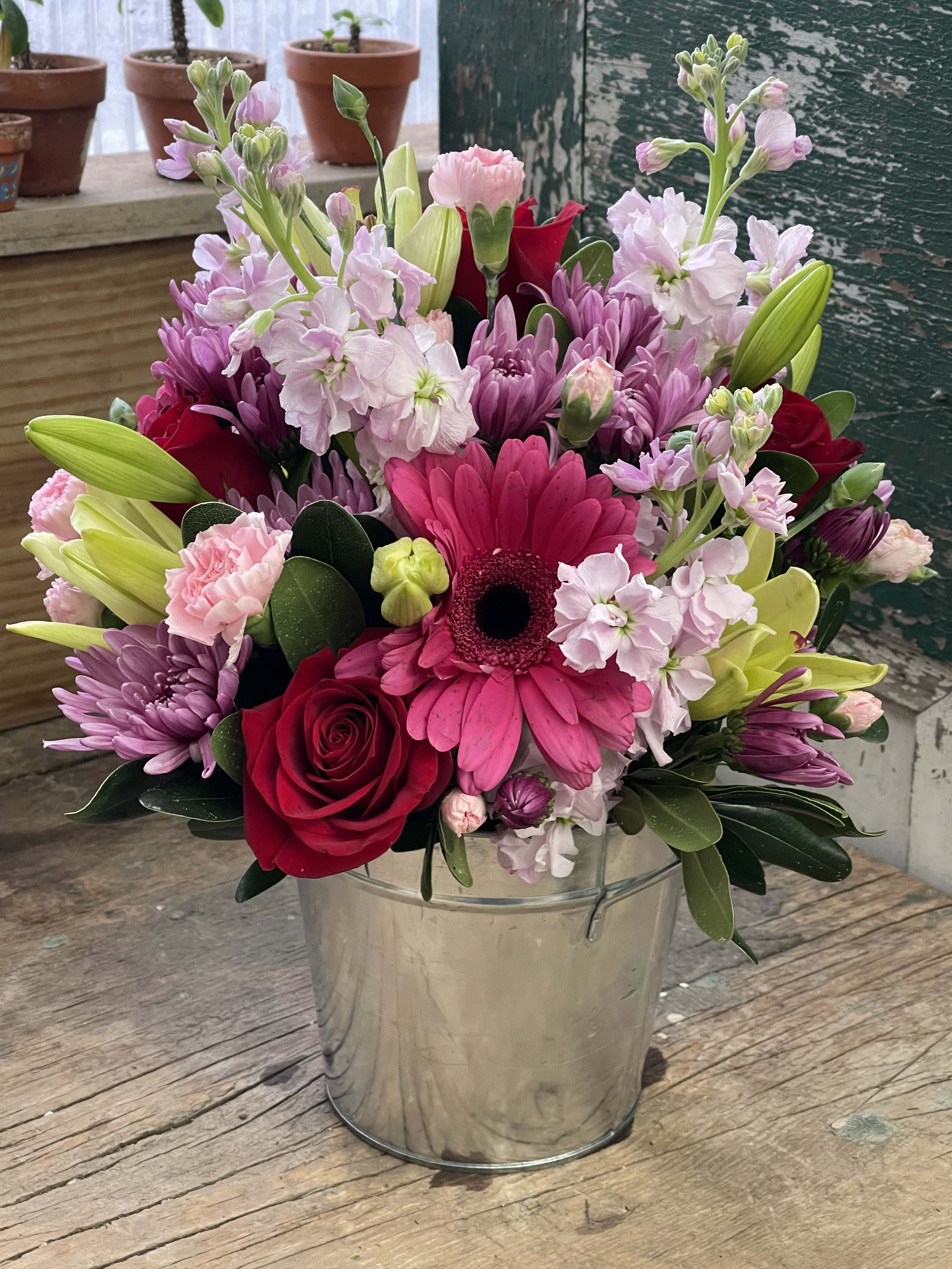 Mixed pink and red flowers arranged in a metal bucket