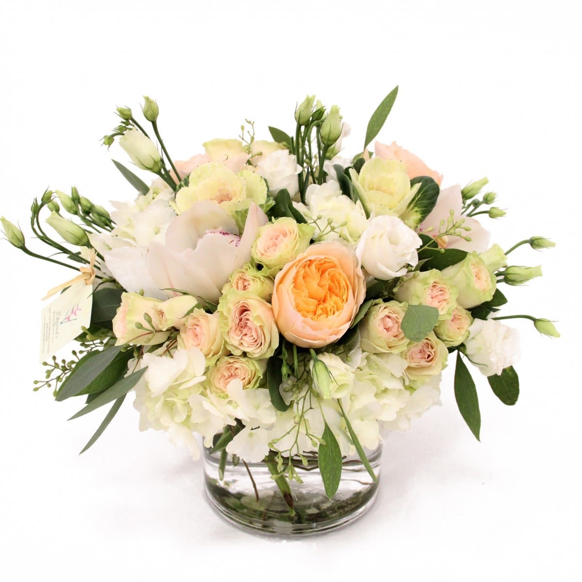 Low arrangement of white hydrangeas, peach roses, and cream blooms in a clear glass vase