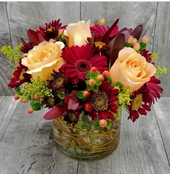 Low arrangement of peach roses and dark red gerbera daisies in a clear glass vase