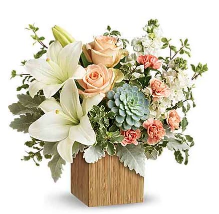 Desert Sunrise Bouquet - Reminiscent of a desert sunrise, this modern mix of peach blooms, white lilies and succulents is a super chic statement in a natural bamboo cube.  Peach roses, white asiatic lilies, peach miniature carnations, and white stock are accented with pitta negra, dusty miller, and a green echeveria succulent. Orientation: One-Sided 