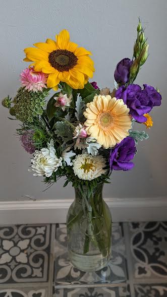 Mixed bouquet with sunflowers, purple blooms, and daisies in a glass vase
