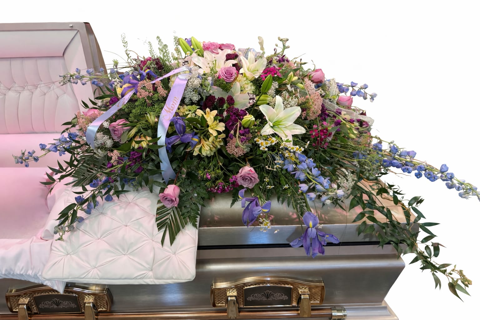 Mother’s Garden - Mother’s Garden is a flowing, garden-style casket spray designed to rest gracefully across the casket. Soft lavender, pink, cream, and blue blooms—including roses, lilies, delphinium, and iris—are layered with lush greenery to create the feeling of a peaceful garden in bloom.  The design moves naturally from end to end, with gentle variation in height and texture that keeps it full without feeling heavy. Delicate butterfly accents add a quiet symbol of remembrance, love, and transformation.  This design was originally created for a family served through Todd Funeral Centre &amp; Crematory, 1600 S State Road 3, Rushville, IN 46173. Families may learn more about Todd Funeral Centre &amp; Crematory at www.toddfuneralcentre.com.  Customers can view additional examples of our custom casket sprays in the Casket Spray section of our website, including real photographs and videos of funeral tributes created by Aspen Tower Florist.  A beautiful choice for honoring a beloved mother with elegance, softness, and natural beauty.  Each arrangement is created with the freshest stems available. Subtle variations may occur while preserving the overall color palette and garden-inspired style.