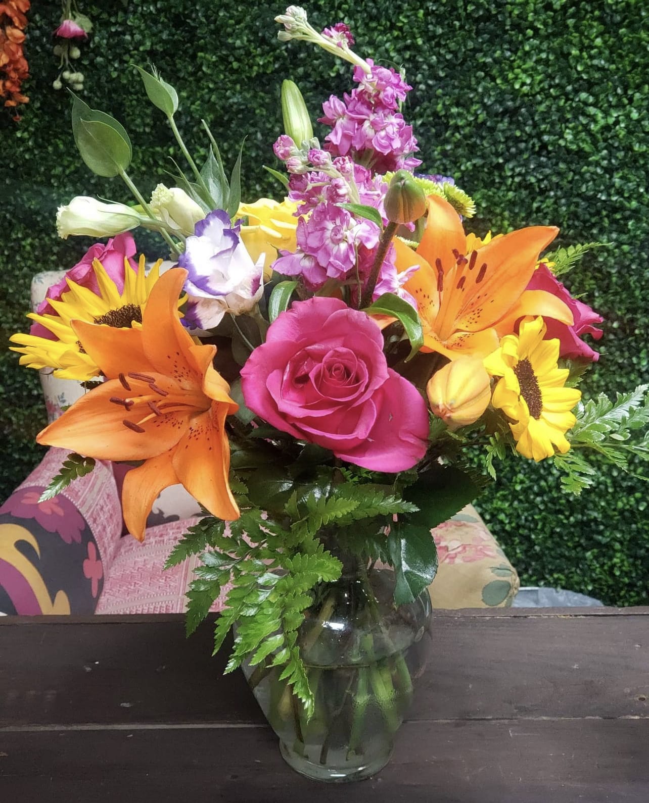 Mixed bouquet of pink roses, orange lilies, and sunflowers in a glass vase