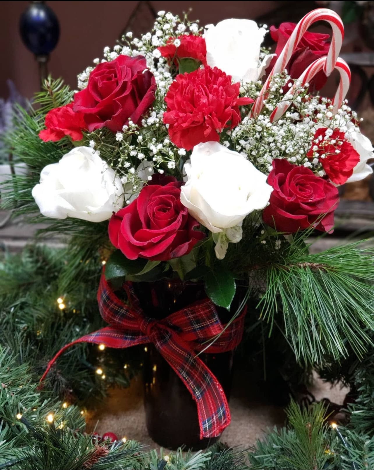 Red and white roses with carnations in a vase, accented by candy canes