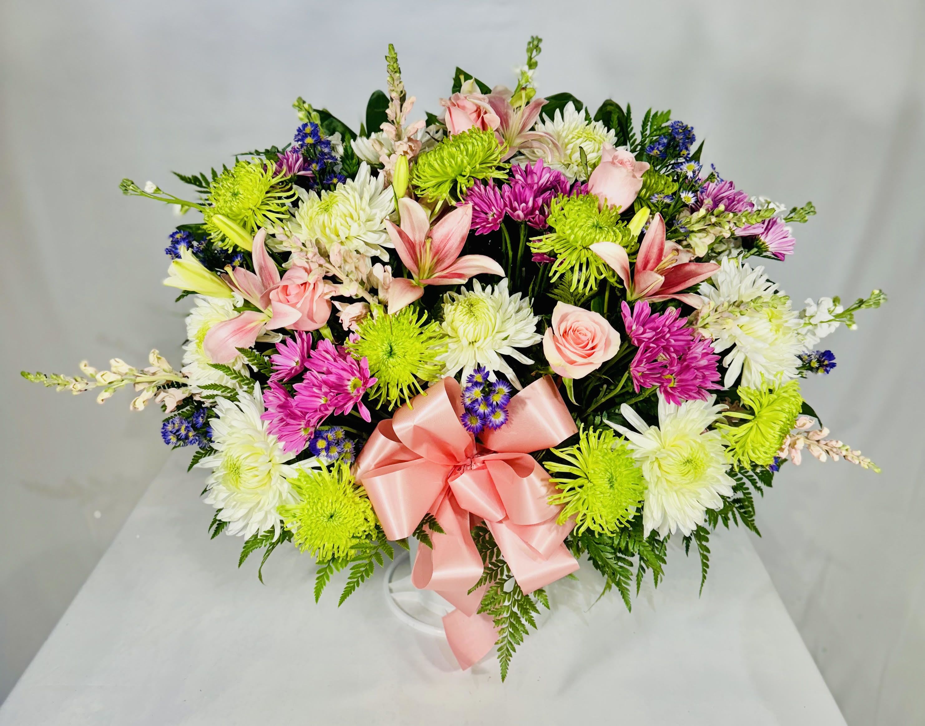 Mixed bouquet with pink lilies, roses, and white and green chrysanthemums tied with a pink ribbon