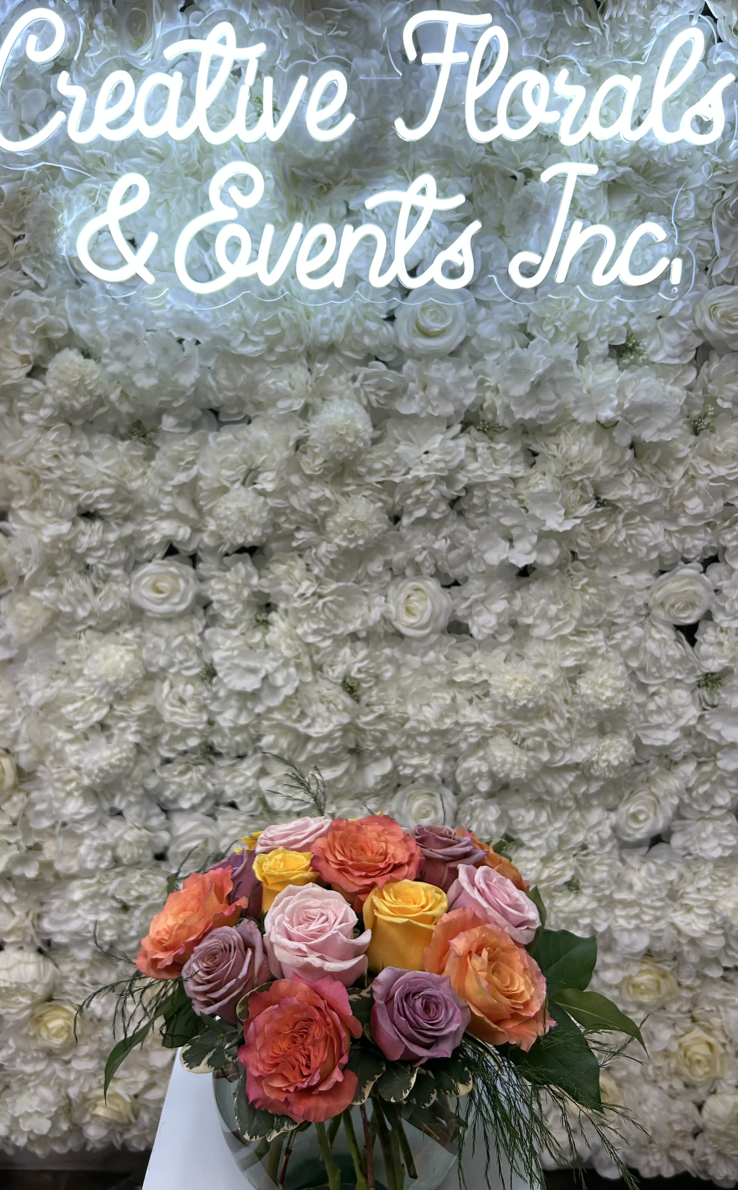 Colorful rose bouquet in a clear vase before a white floral wall
