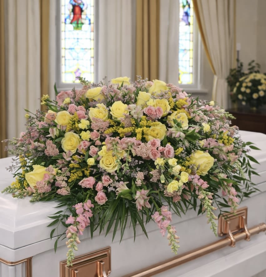 Blushing Meadow Casket Spray - Soft, romantic, and filled with garden-inspired beauty, Blushing Meadow is a lush casket spray designed to honor a loved one with warmth, grace, and remembrance. Featuring a blend of soft pink and buttery yellow flowers accented with fresh greenery, this design creates a natural and comforting tribute that feels elegant without being overly formal.  Roses and complementary blooms are layered throughout the arrangement to create texture, movement, and fullness across the casket. The gentle color palette symbolizes love, friendship, cherished memories, and a life beautifully lived. Flowing greenery softens the design and enhances its fresh garden appearance.  Blushing Meadow is an excellent choice for funeral services, memorial gatherings, visitation services, and celebration-of-life events. Its soft colors and relaxed styling make it especially appropriate for families seeking a tribute that feels peaceful, loving, and uplifting.  Designed to create a beautiful focal point while honoring a cherished life, this arrangement offers a heartfelt expression of remembrance and enduring affection.  Suitable for services at Myers Funeral Home, Neal’s Funeral Home, and Freeman Family Funeral Homes.  Available through Aspen Tower Florist for families in Rushville, Milroy, and Shelbyville seeking casket sprays, funeral flowers, memorial tributes, and sympathy arrangements.