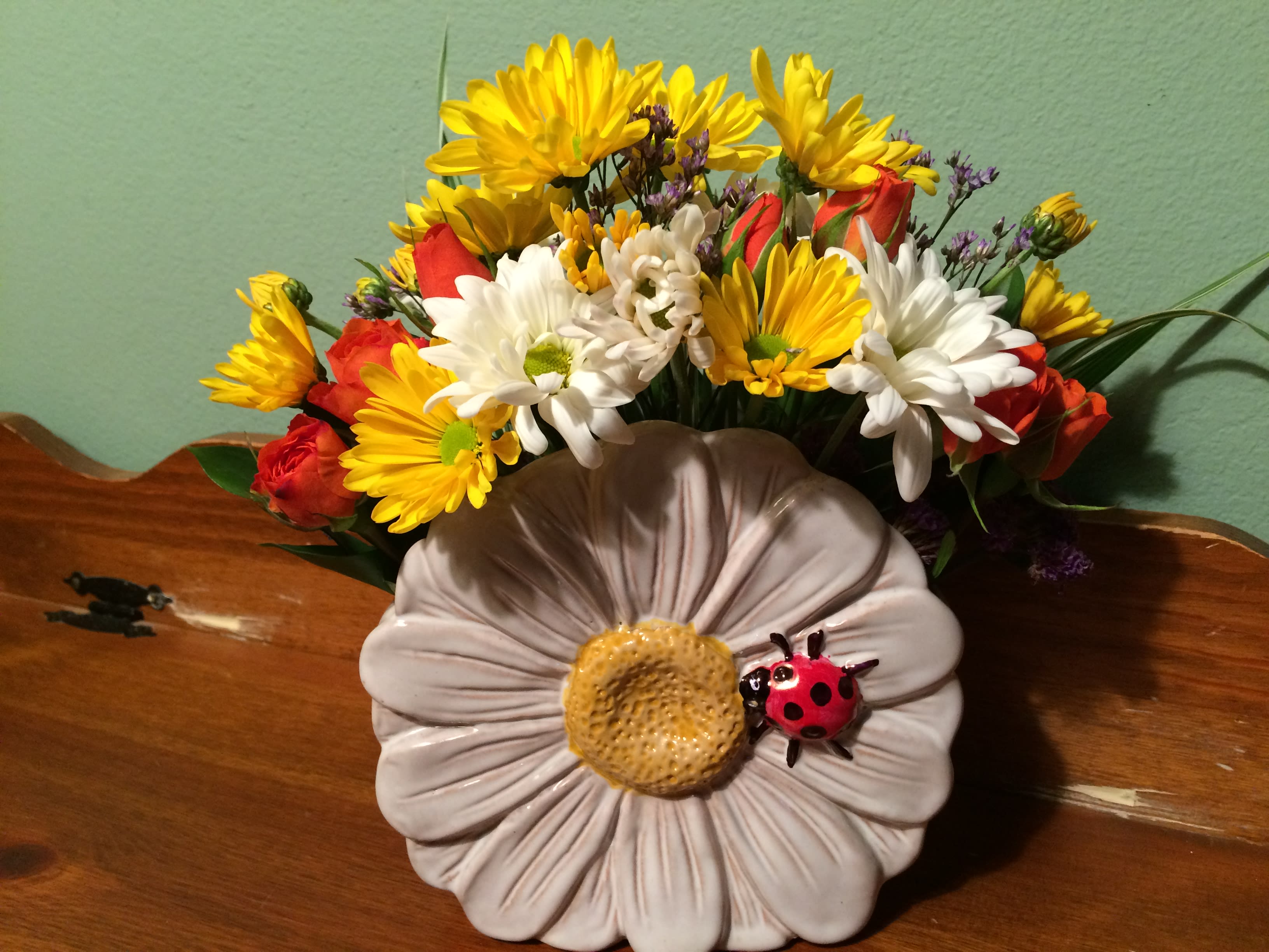 Mixed bouquet of yellow and white daisies with red roses in a decorative vase